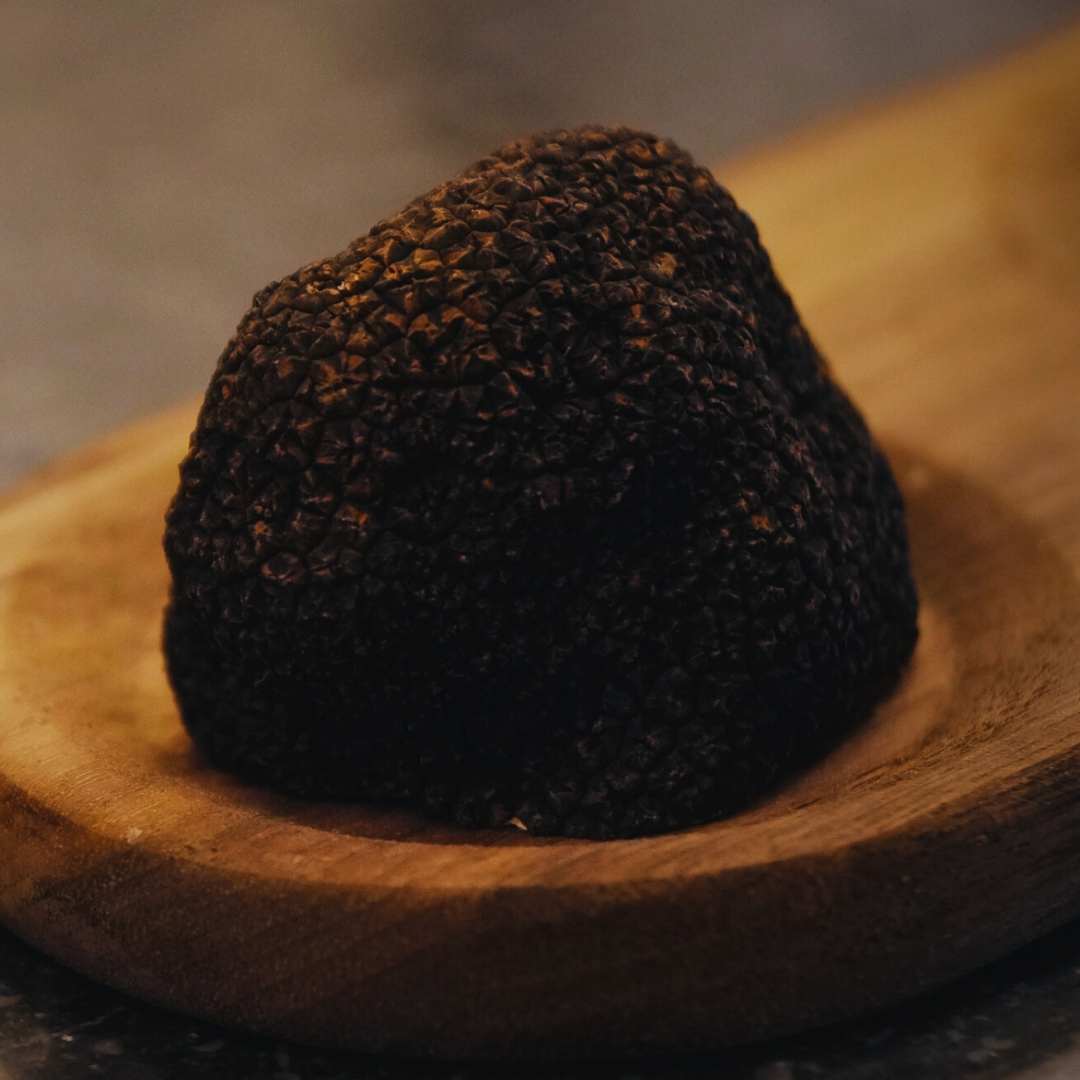 A close-up of a black truffle on a wooden surface.