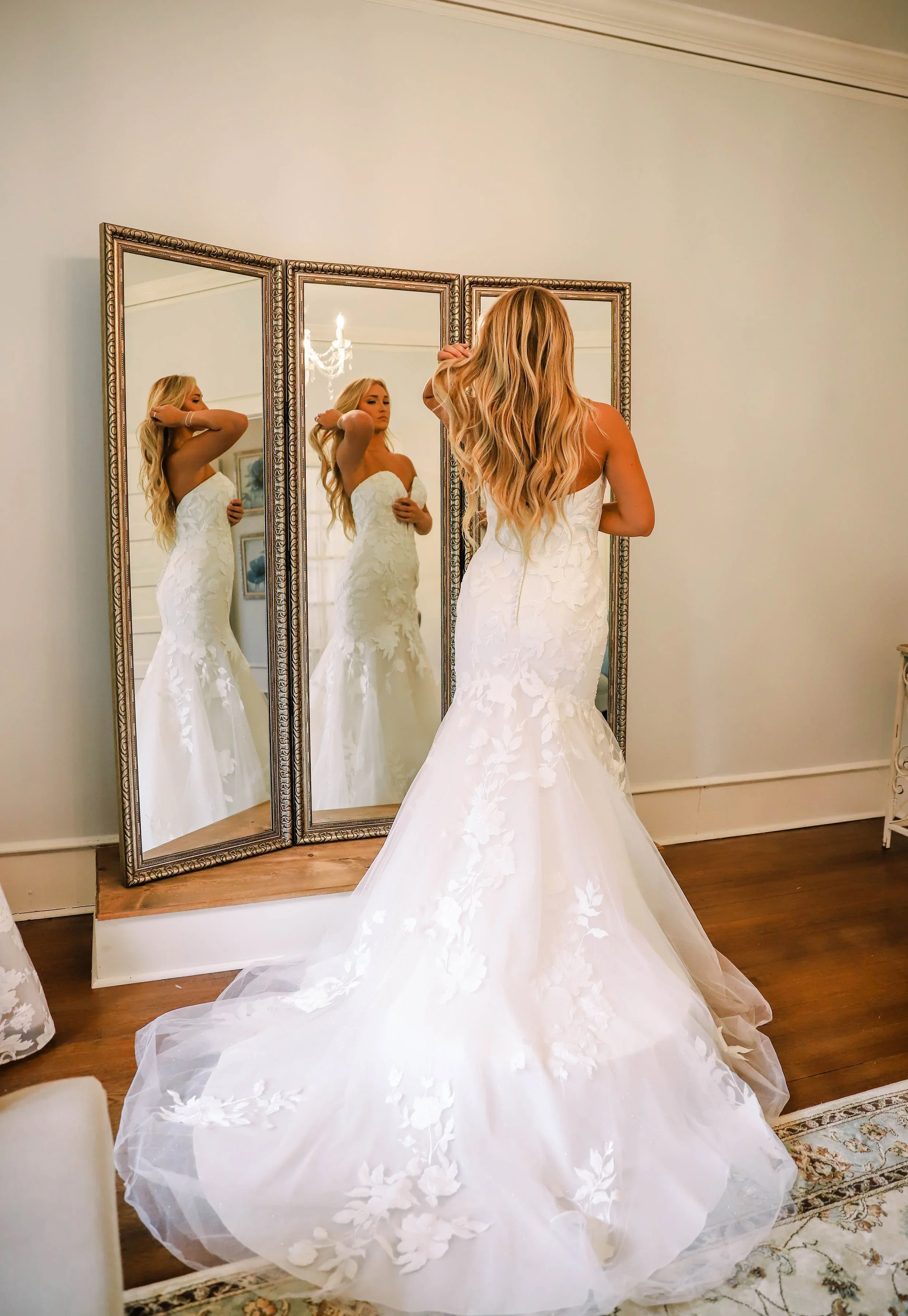 Bride wearing a strapless lace fit-and-flare wedding dress with floral appliqués and a chapel-length train, posing in front of a three-panel mirror at Atlanta Street Bridal Boutique