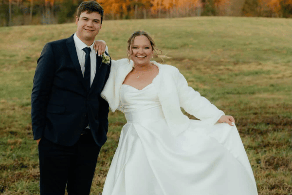 Bride and groom posing outdoors after their wedding, with the bride wearing a long-sleeve modest wedding dress.