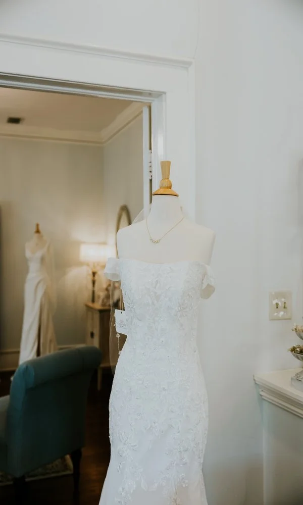 Off-the-shoulder lace wedding dress on mannequin inside Atlanta Street Bridal boutique with elegant showroom setting.