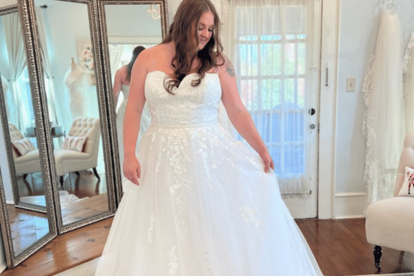 A bride trying on her strapless wedding gown, one hand holding her dress, the other hand at the side, door and mirror as her background