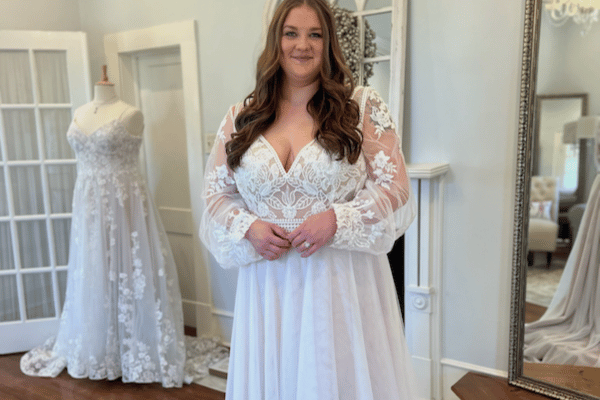 A bride trying on her white wedding dress with lace long sleeves, with mirror and mannequin in her background