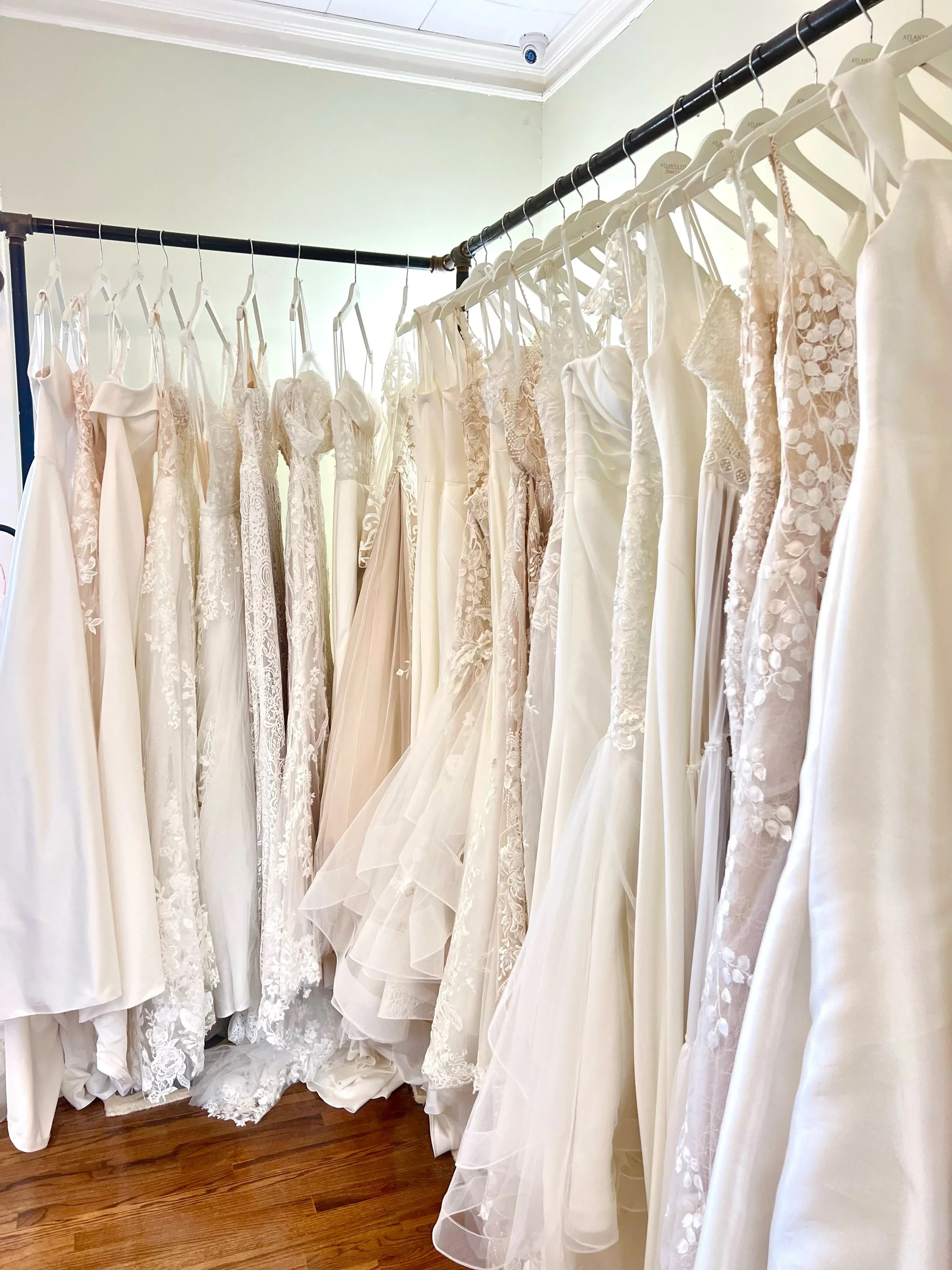 selection of wedding gowns in various silhouettes and fabrics, including lace, satin, and tulle, displayed on hangers inside Atlanta Street Bridal Company