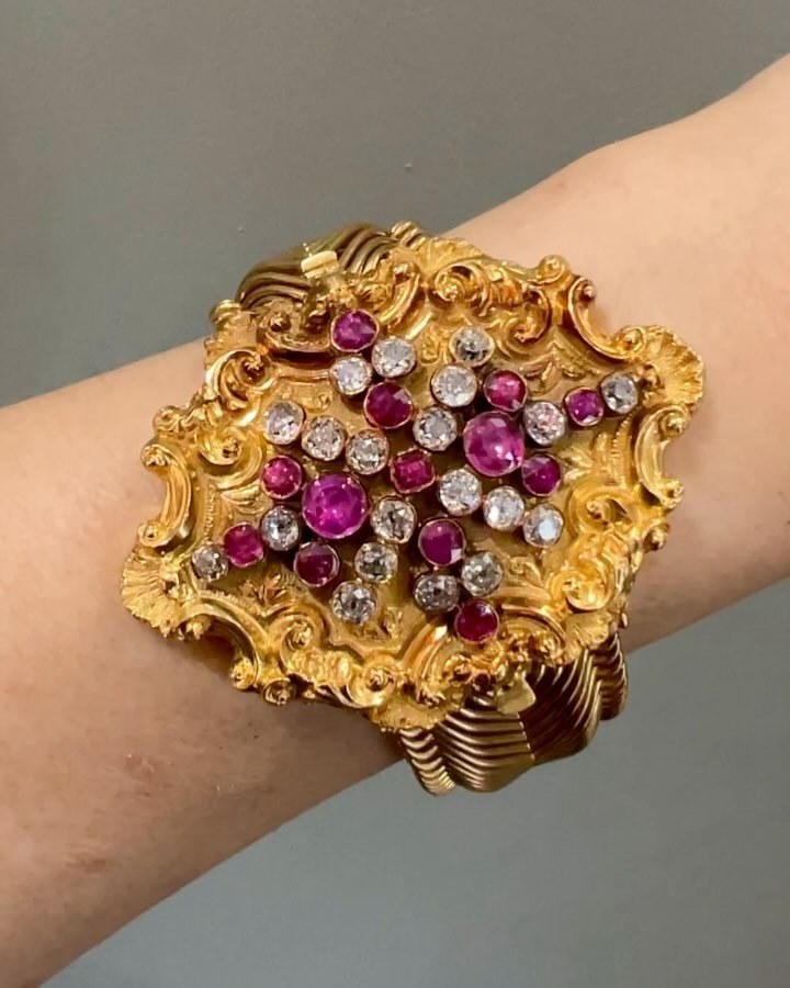 An antique ruby and diamond bracelet, English, c. 1860, the repousse scroll and shell chased panel set with an open cluster of cushion shaped rubies and old mine cut diamonds on an articulated open wire scroll band, detcheable with additional brooch 