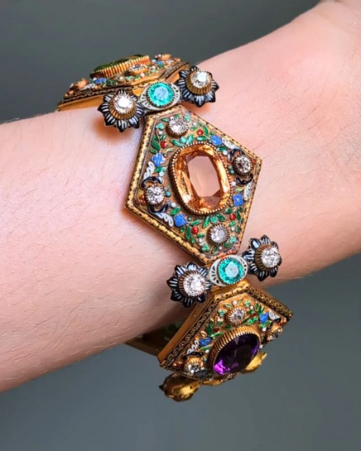 An antique diamond, gem set and enamel gold bracelet designed as a series of five lozenge shaped panels with polychrome foliate enamel and diamond detail each set with peridot, amethyst, topaz and hessonite garnet respectively, mounted in 18kt gold. 