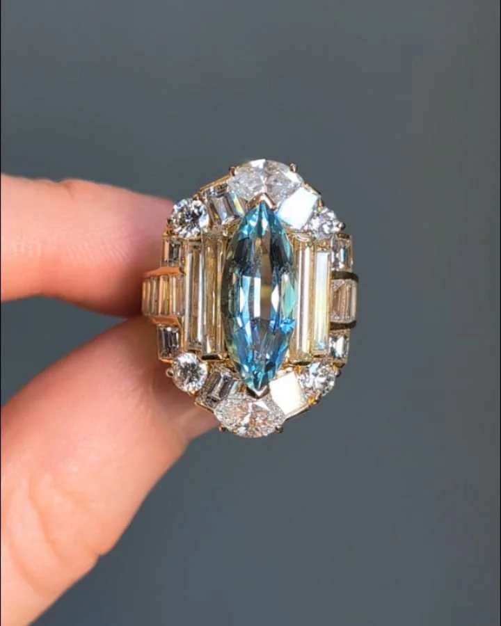 An aquamarine and diamond ring, the central navette shaped aquamarine within a circular, baguette and marquise cut 18kt gold mount. Circa 1980. Available @simonteaklejewelry #aquamarinering #vintageaquamarine #vintageaquamarinering #vintageaquaring #
