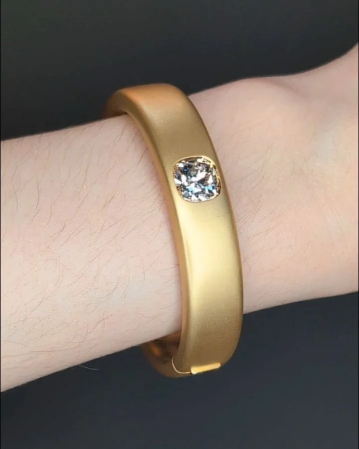 An 18kt gold and diamond bangle, the central 4.35 cts cushion shaped diamond set in a plain matte finish band. Available @simonteaklejewelry #goldanddiamondbangle #cushiondiamond #diamondbangle #contemporaryjewelry #simonteaklejewelry #simonteakleava
