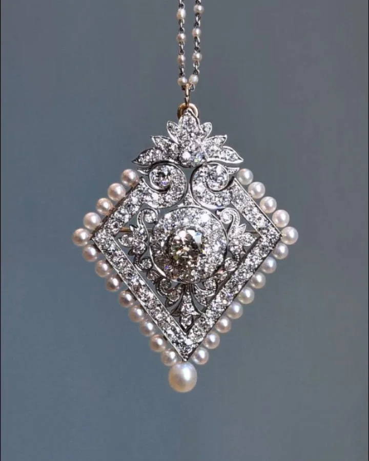 A Belle Epoque pearl and diamond pendant, of open lozenge form, the central circular cluster with an open scroll surround, with a two tiered diamond and natural pearl border, mounted in gold and platinum, and a platinum and seed pearl chain. Circa 19