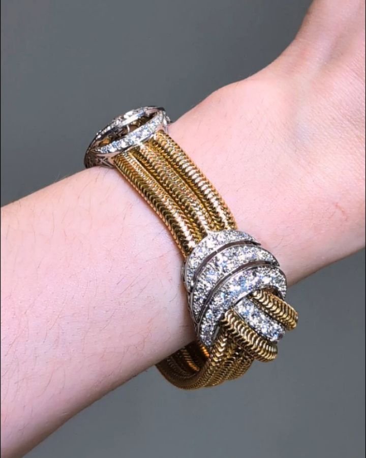 A Retro diamond bracelet, designed with two circular cut diamond scroll knot motifs connected by three brazilian link bands, mounted in 18kt gold and platinum. Circa 1950. Available @simonteaklejewelry #retrobracelet #retrogoldbracelet #retrodiamondb