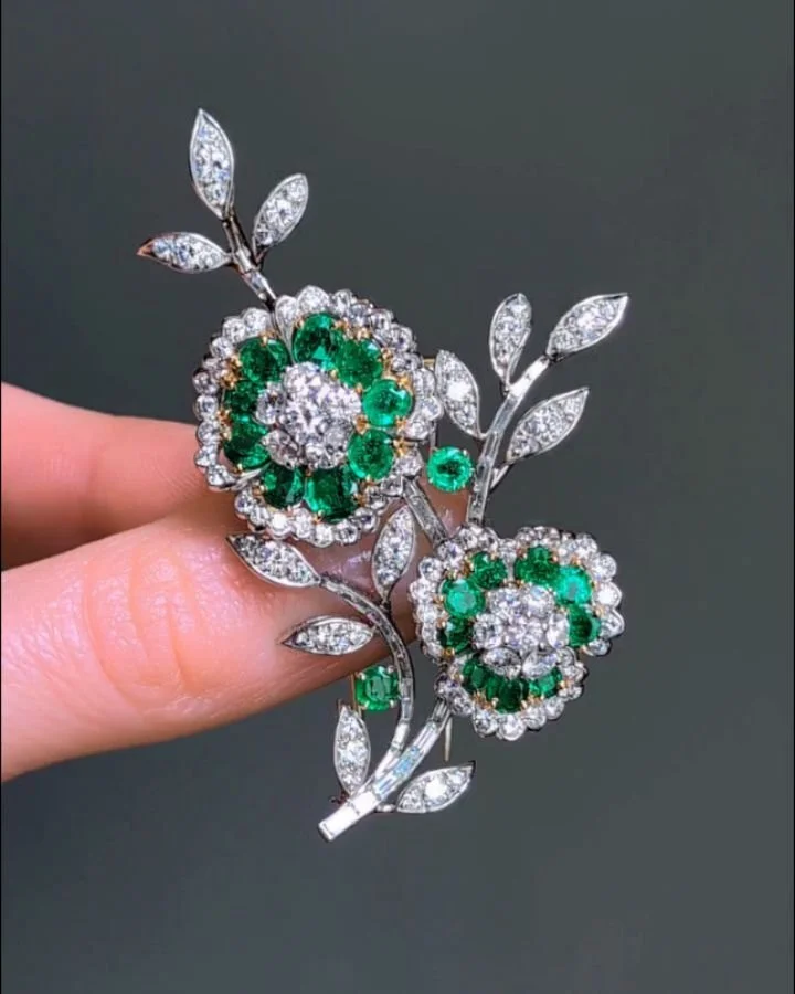 An emerald and diamond floral spray brooch by Van Cleef &amp; Arpels, designed with two sculpted emerald and diamond circular flower heads with a diamond set spray and stem, mounted in platinum. Circa 1955. Available @simonteaklejewelry #vancleefarpe