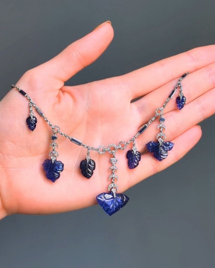 An Art Deco sapphire and diamond necklace, designed as a fringe of foliate carved sapphires suspended from a chain necklace with crescent and open circle motifs mounted in platinum. Circa 1920. Available @simonteaklejewelry #artdecojewelry #artdecoje