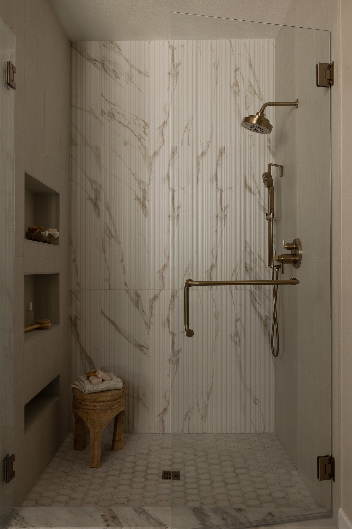 Elegant and sophisticated bathroom shower with reeded tile and brass plumbing fixtures.