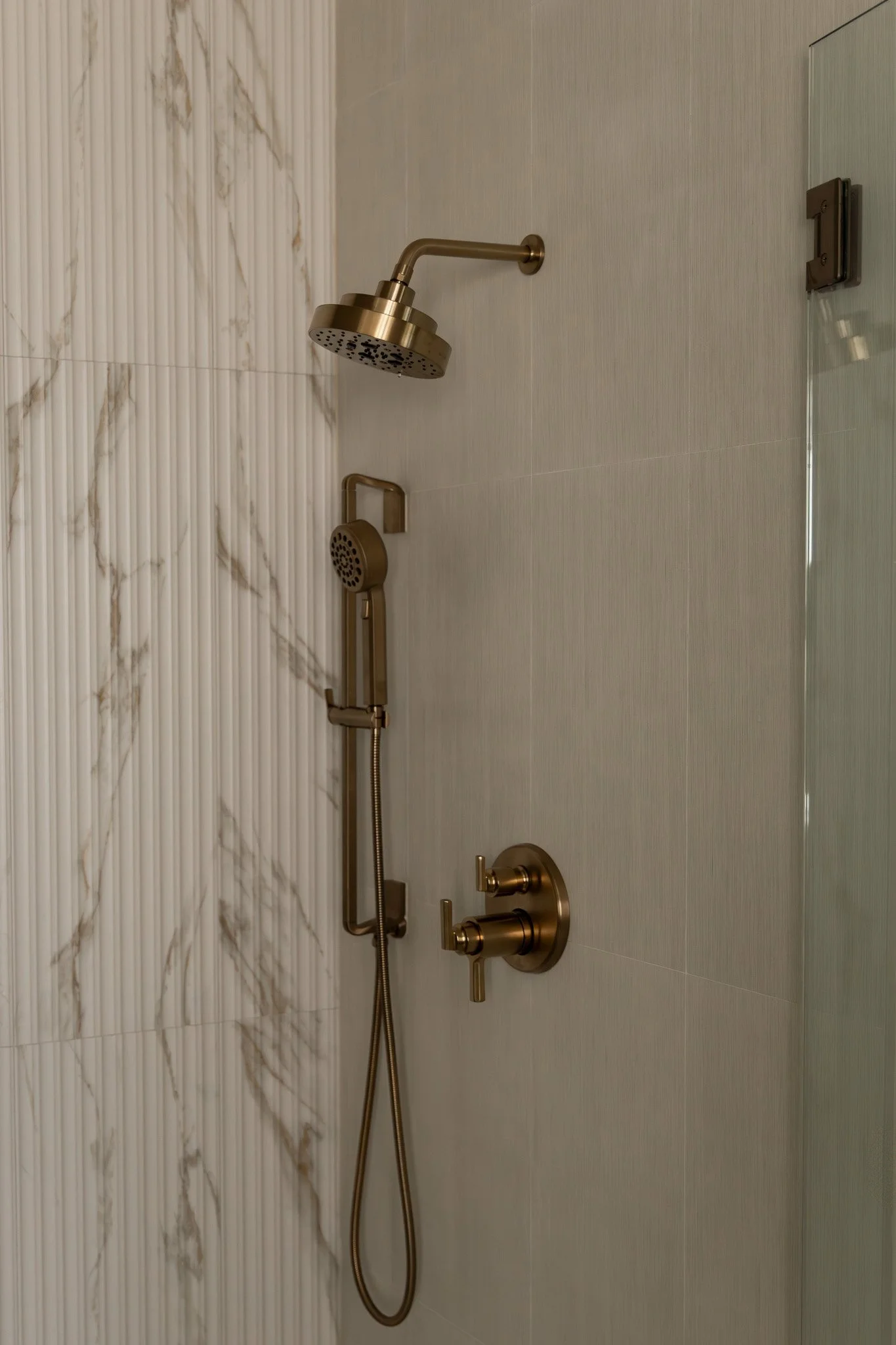 Elegant and sophisticated bathroom shower with reeded tile and brass plumbing fixtures.