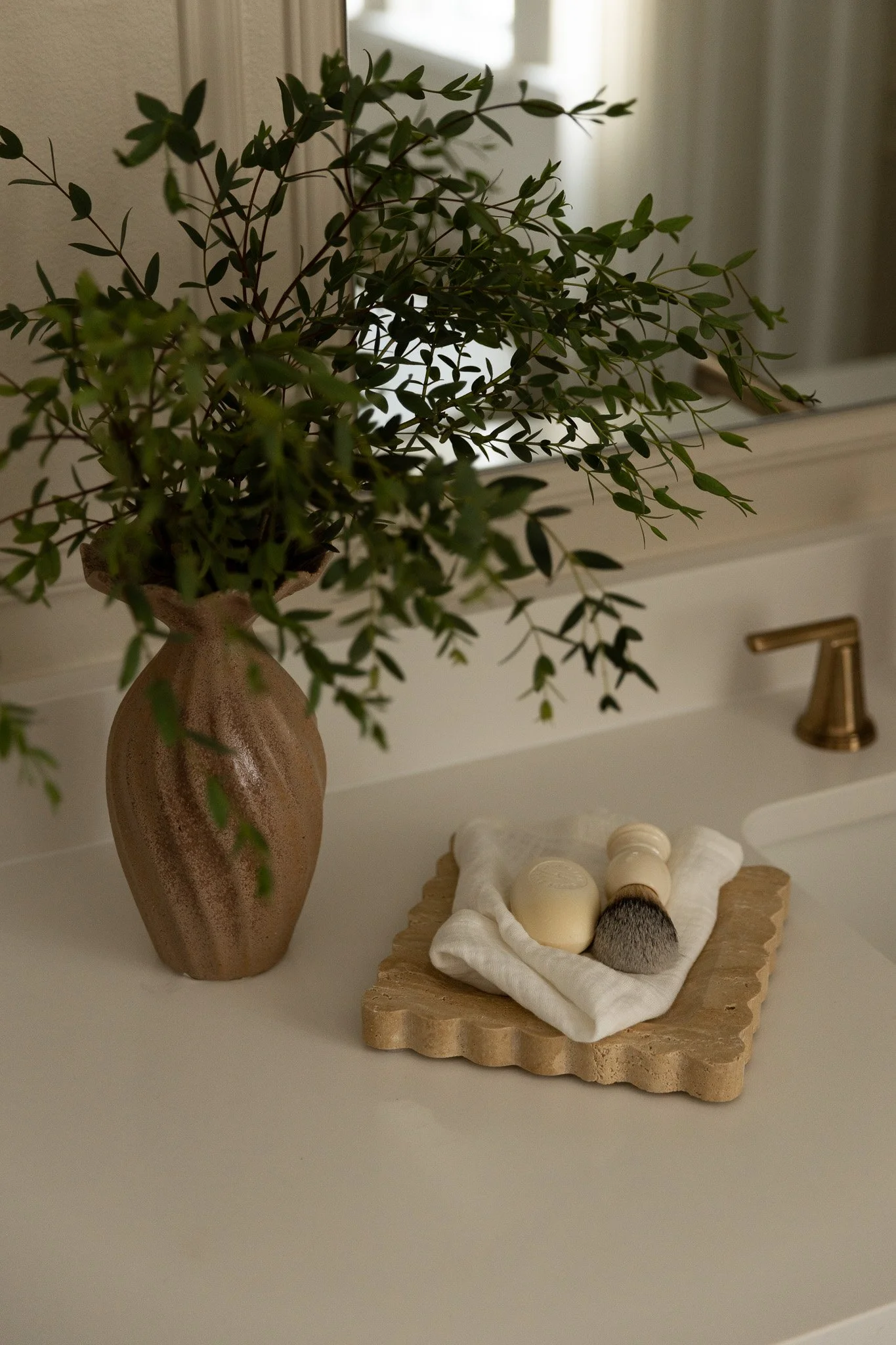A close up shot of elegant bathroom accessories featuring vase, branches, floral greenery, soap, marble tray, towels.