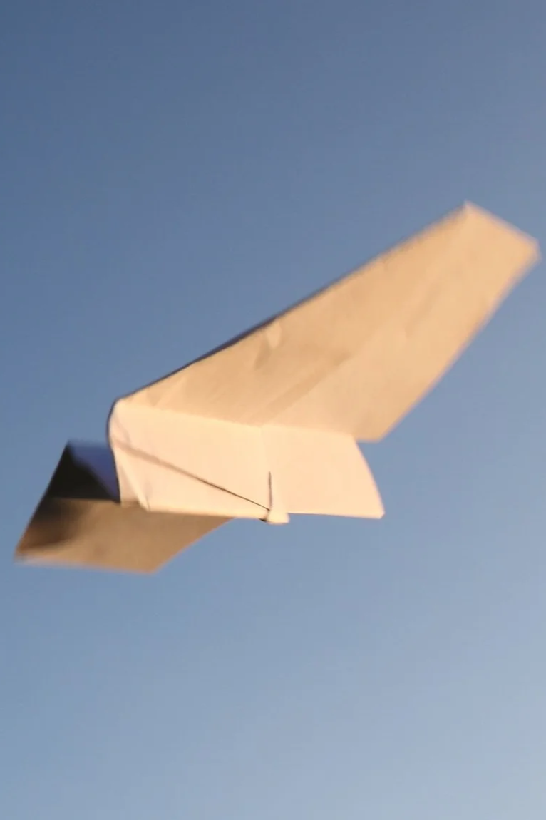 Two hands connecting two white puzzle pieces outdoors on green grass.