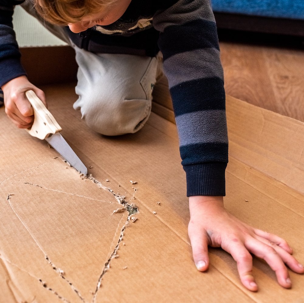 child-playing-with-a-cardboard-box-and-a-saw-to-bu-2023-11-27-04-48-53-utc.JPG