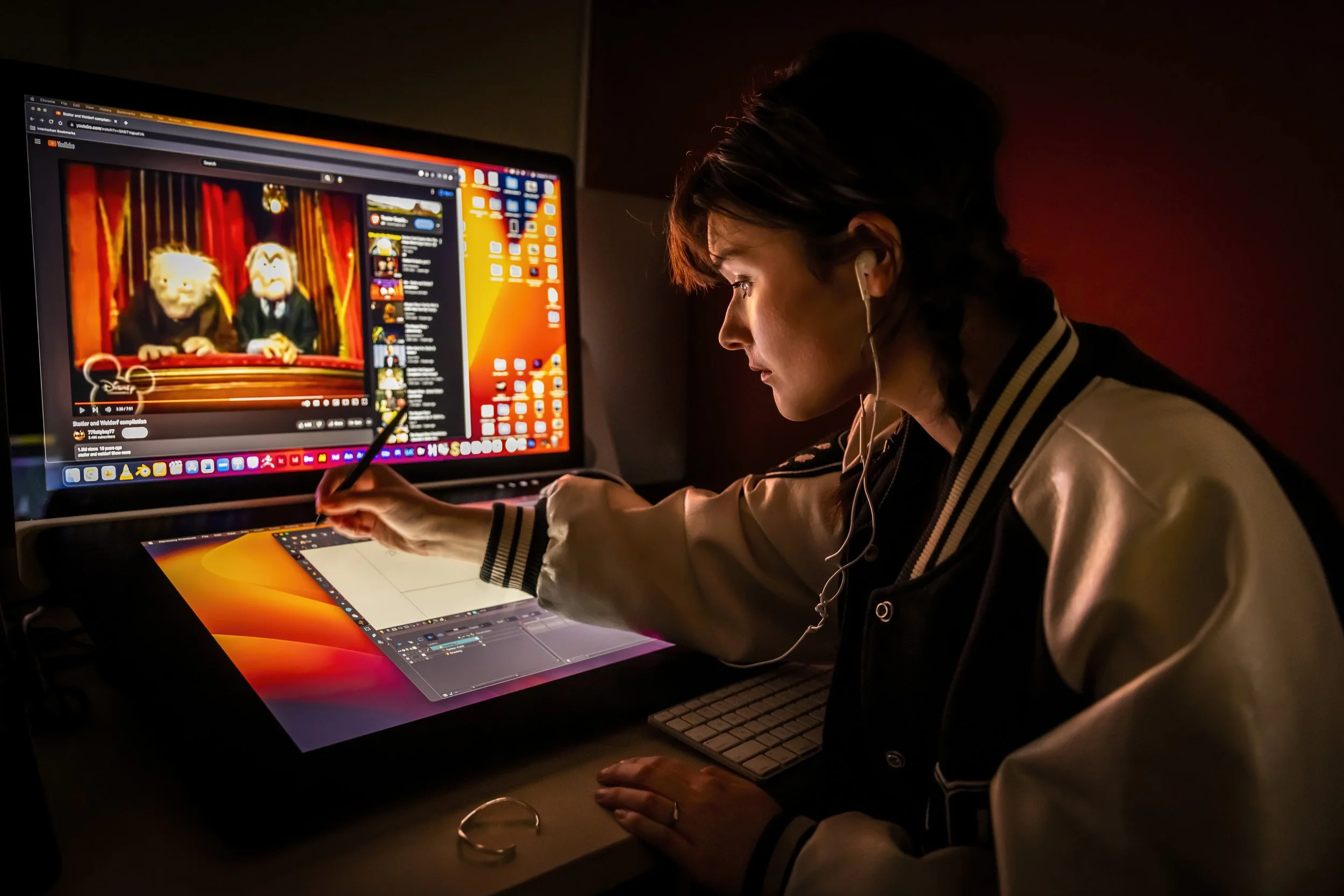 Person working on a computer in a dark room, with a large screen displaying a stop-motion animation of two puppets and a desktop with various icons.