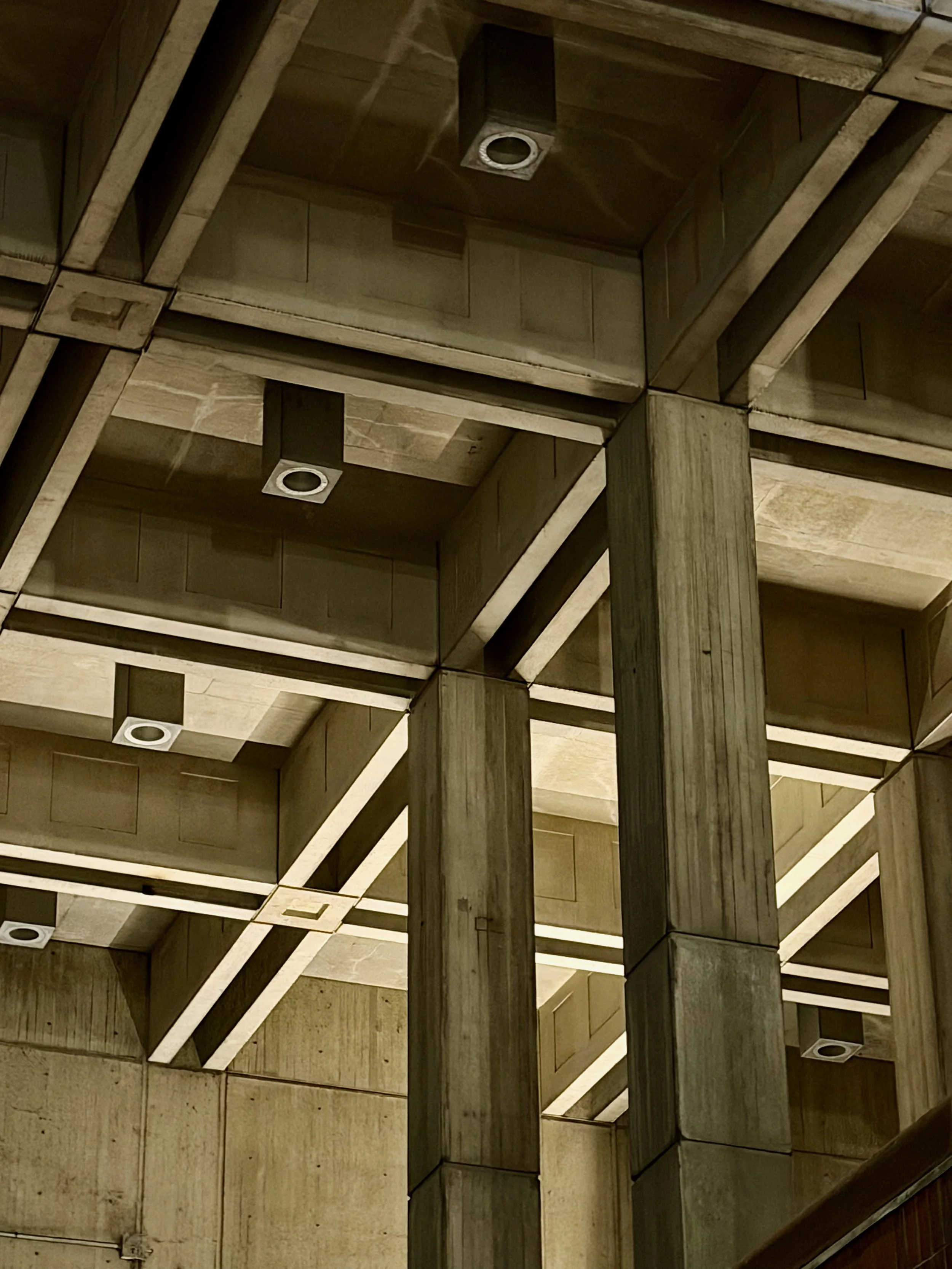 Multiple square wooden blocks arranged in a grid pattern on a wooden ceiling, with embedded square light fixtures and wooden support columns.