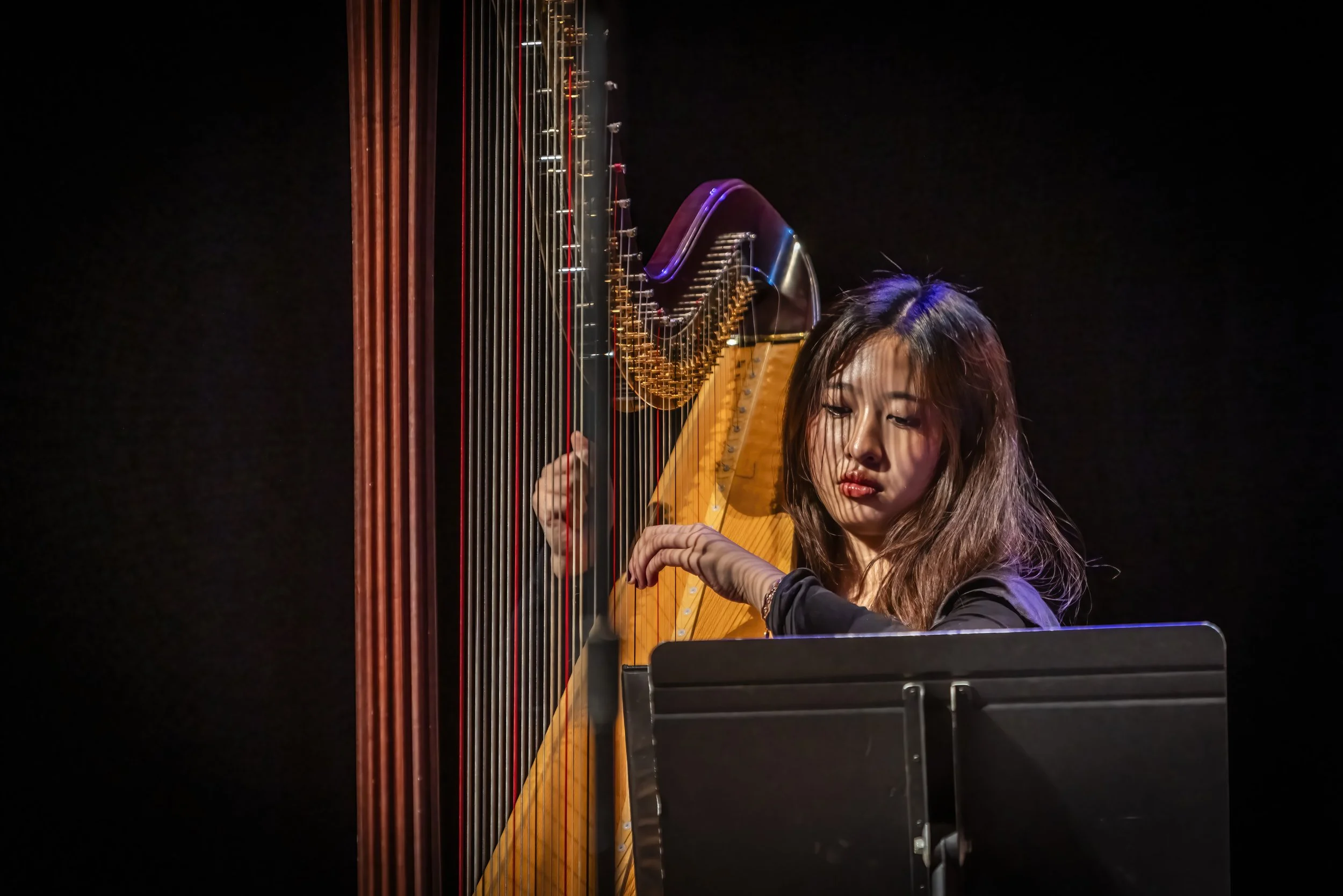 A woman playing a harp and a guitar on a dark stage.