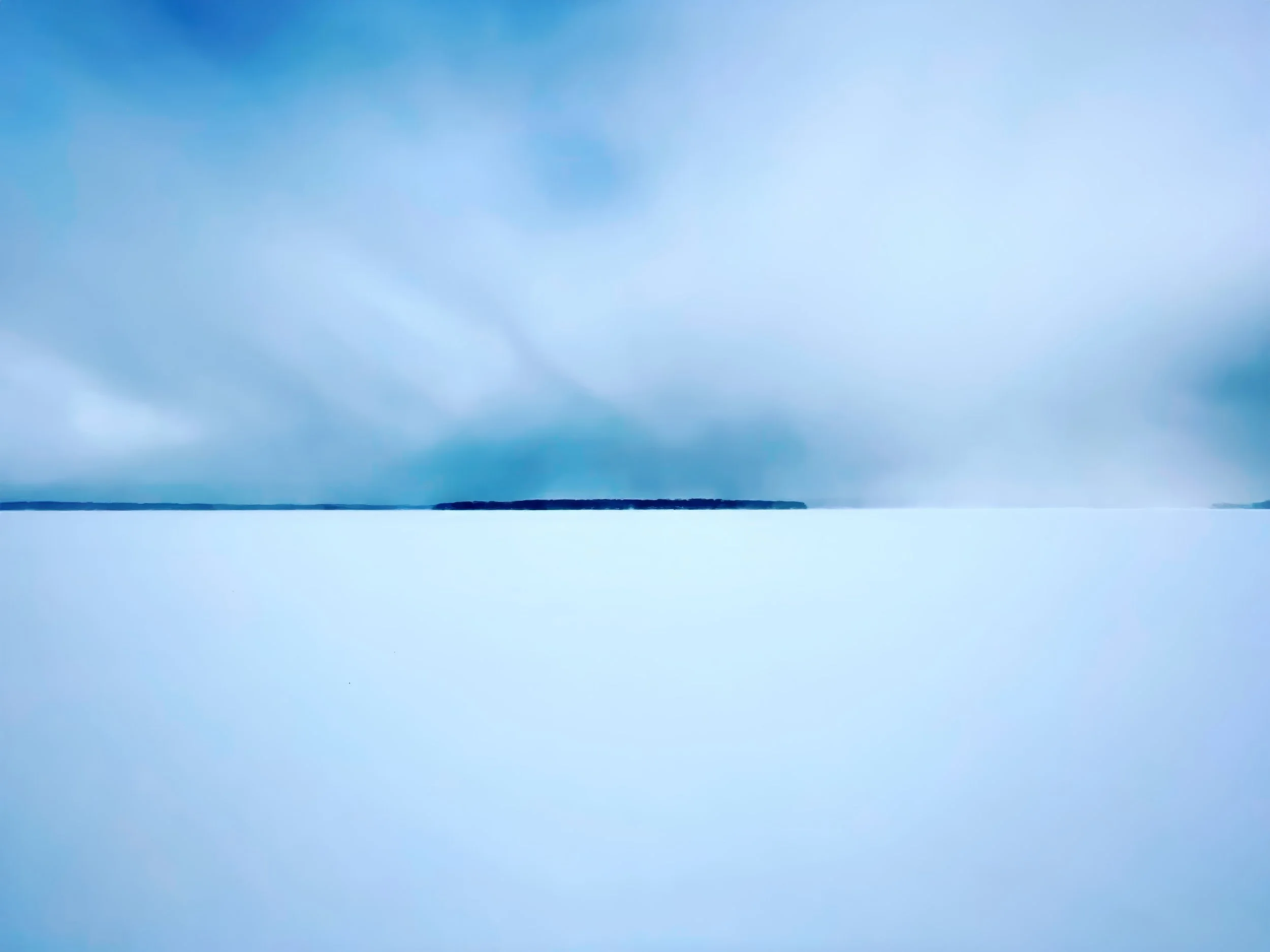 A snowy landscape with a distant row of trees under a cloudy sky.