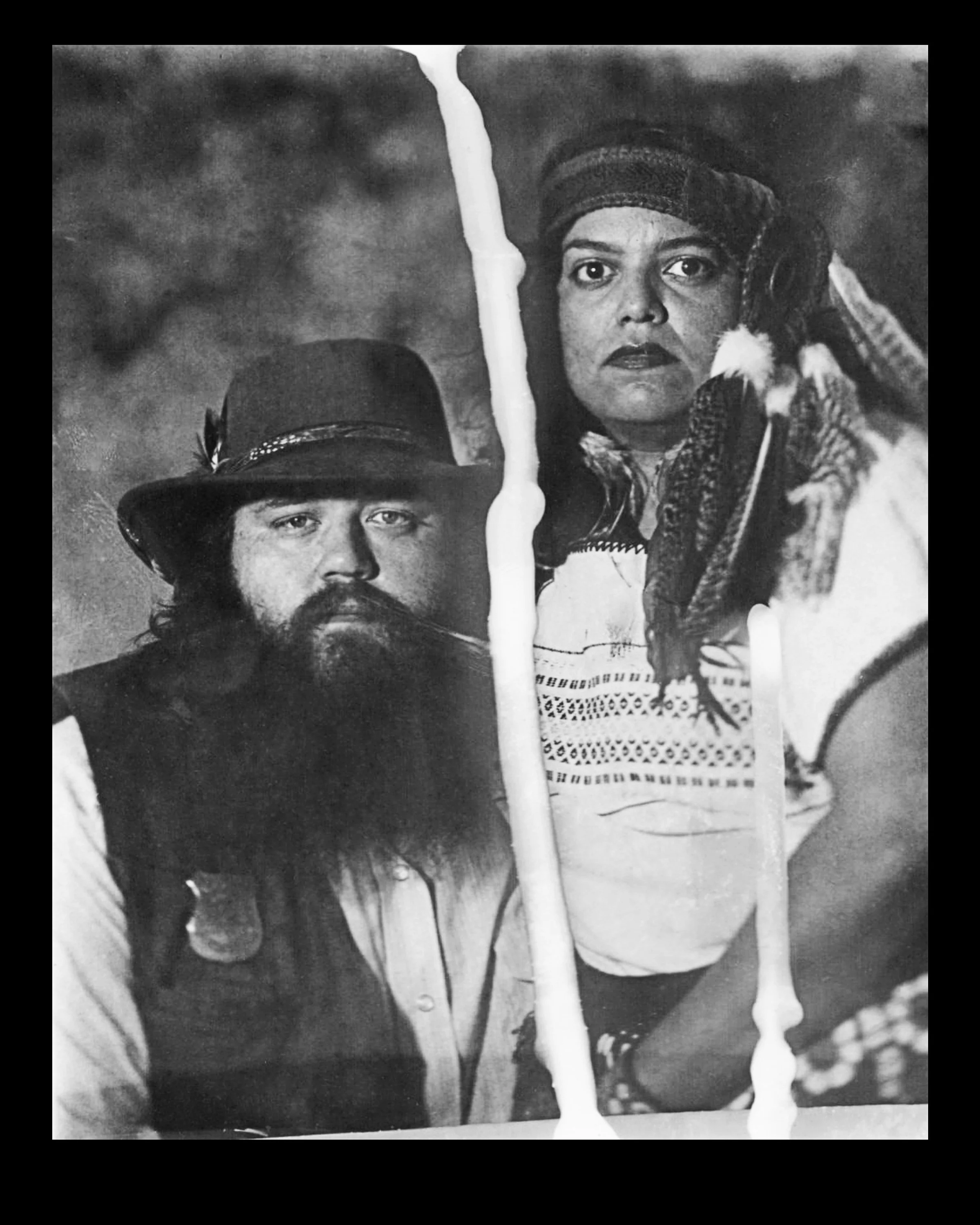 Black and white photograph of a man with a beard wearing a hat, and a woman with patterned clothing and braided hair, holding candles.