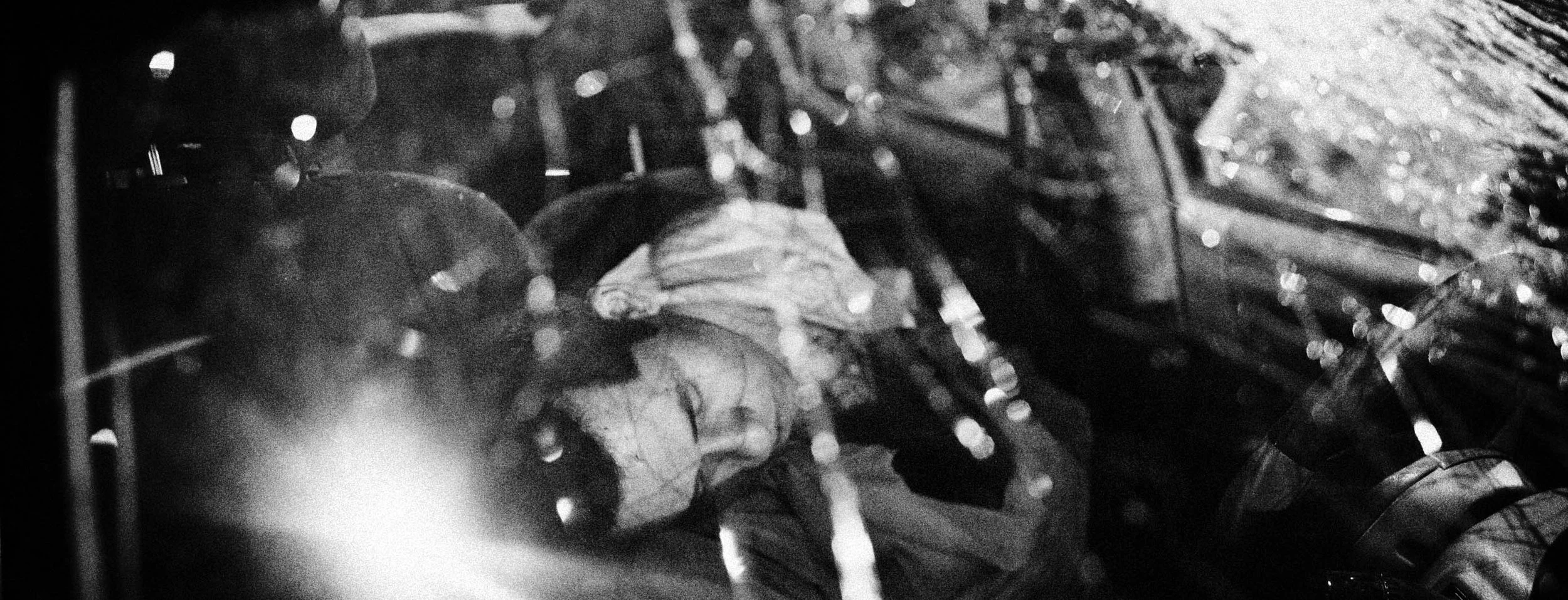 Black and white photo of a face with closed eyes, partially obscured by shimmering lights and reflections.