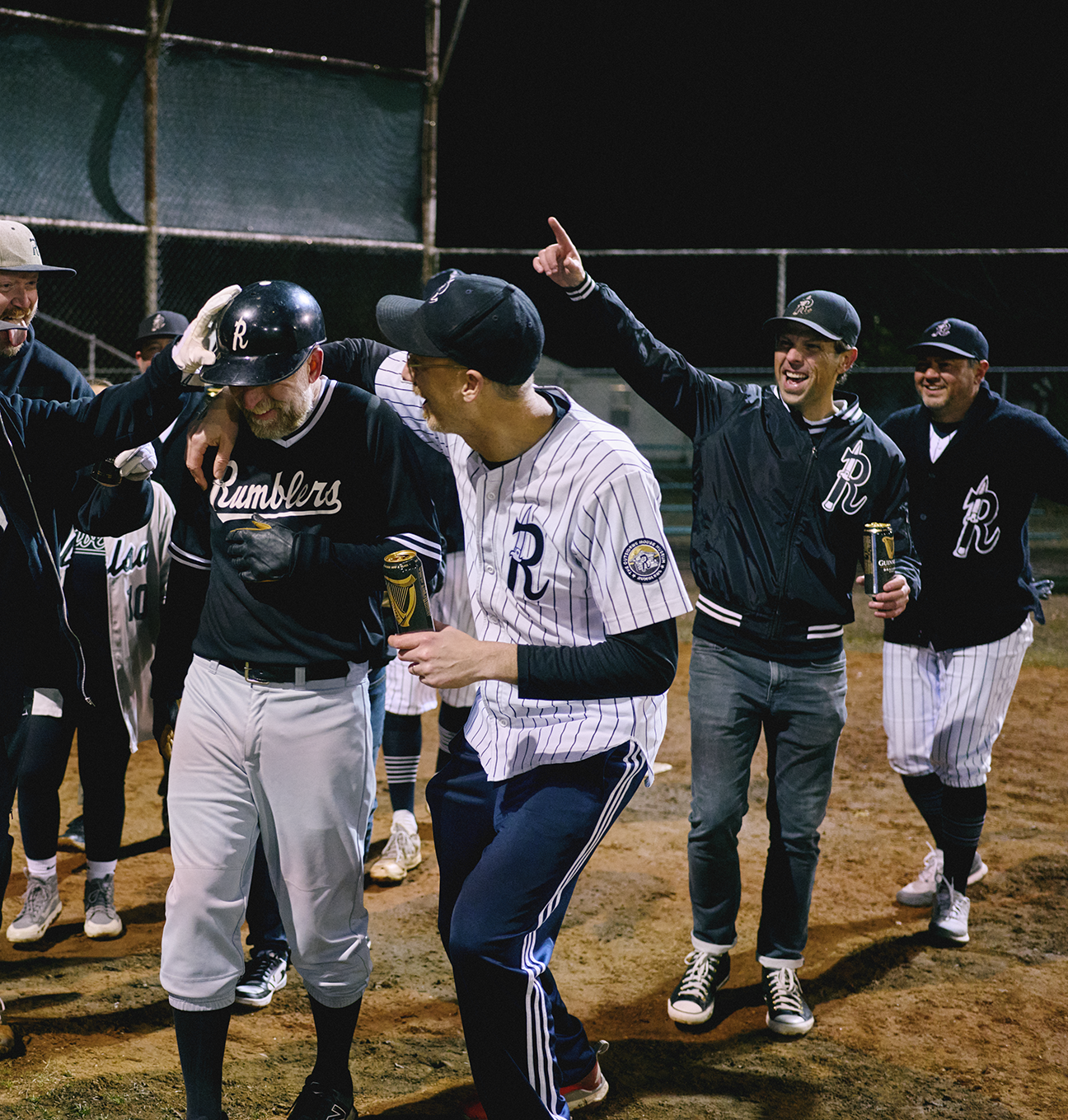 A group of baseball players on the field celebrating at night, wearing team uniforms drinking Guinness beer.