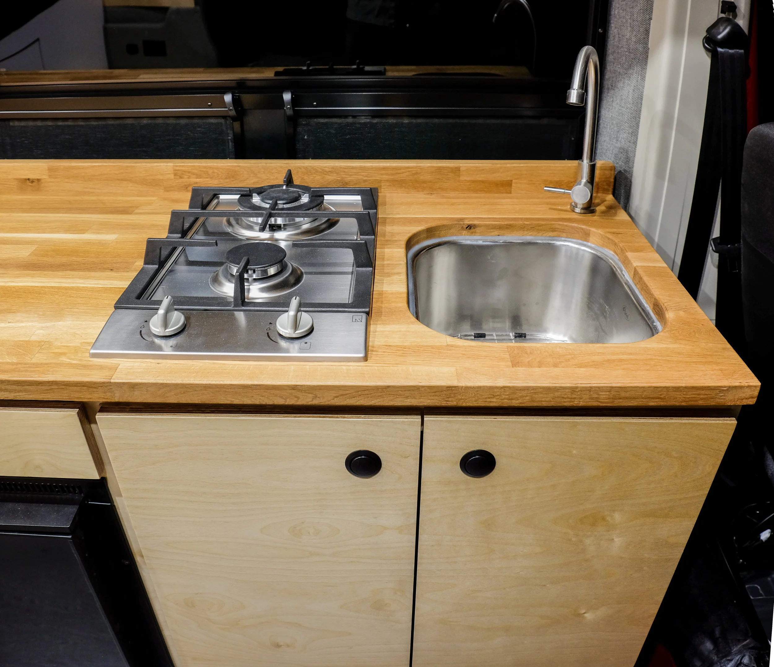 Under the kitchenette's oak butcher block countertop is a 7 gallon fresh-to-grey water system and an 11-lb propane tank. The propane fuels the two-burner cooktop as well as the rear-mounted shower system. Above the Isotherm refrigerator is a touch-to-open cutlery drawer. The dual vented window behind the kitchenette allows for some nice airflow (and a great view) while cooking. 