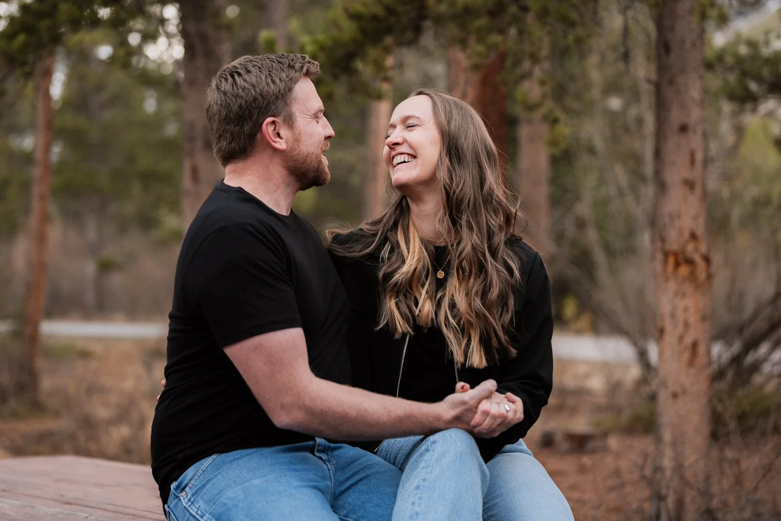 Couple laughing together during a candid engagement session in the pine trees near Red Lodge Montana