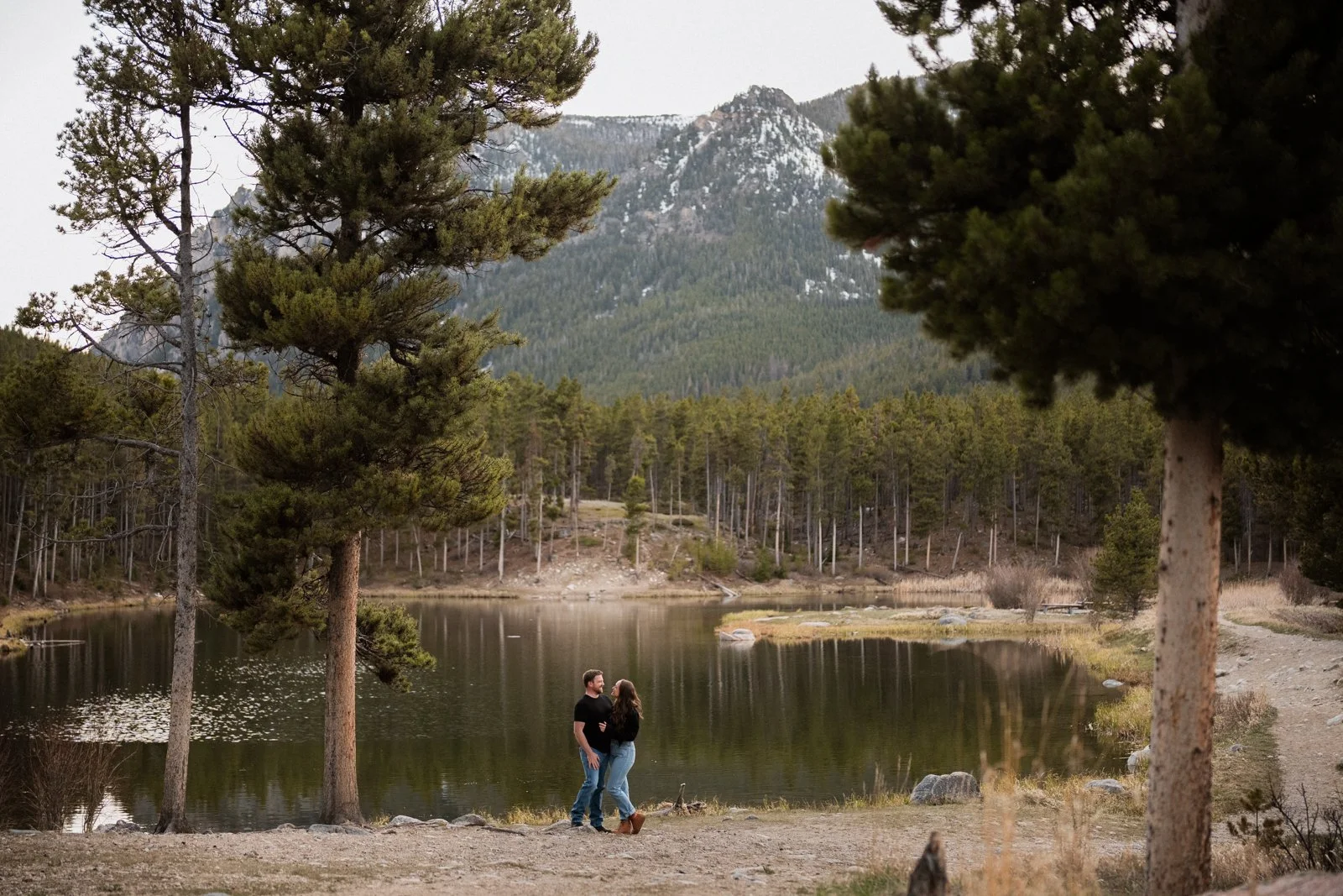 Couple standing beside a mountain lake during an engagement session near Red Lodge Montana