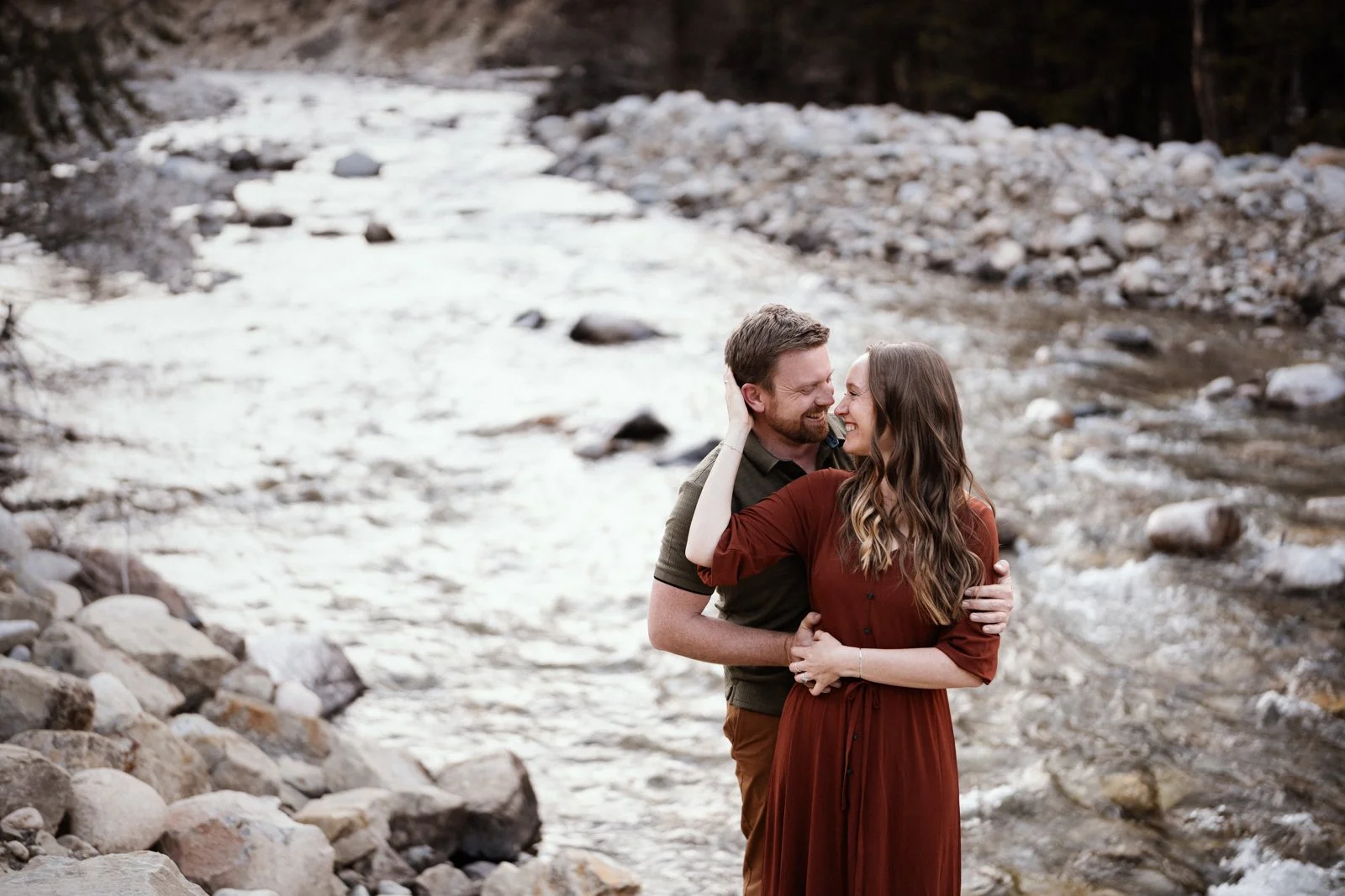 Couple embracing beside a mountain creek during an engagement session near Red Lodge Montana