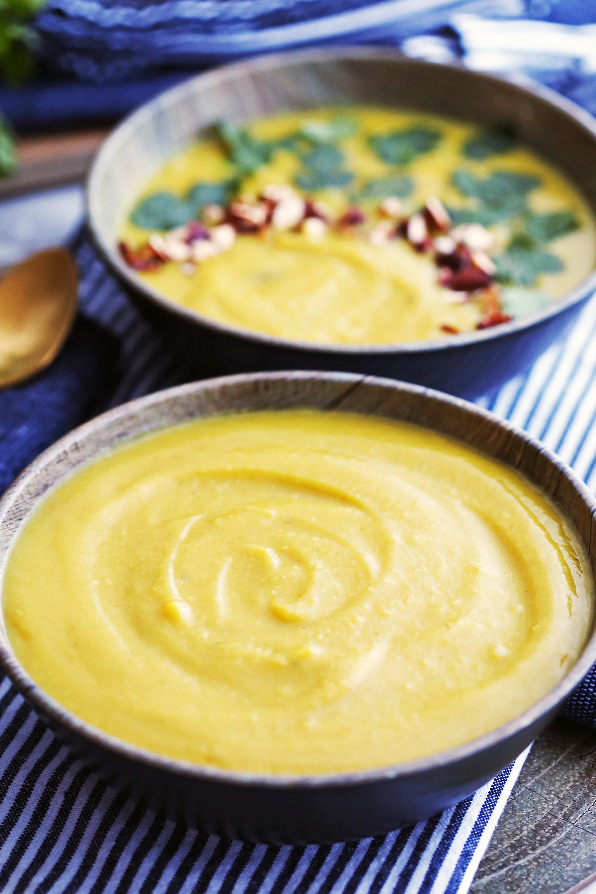 Creamy Turmeric Cauliflower Potato Soup in two dark-brown bowls, one placed in front of the another.