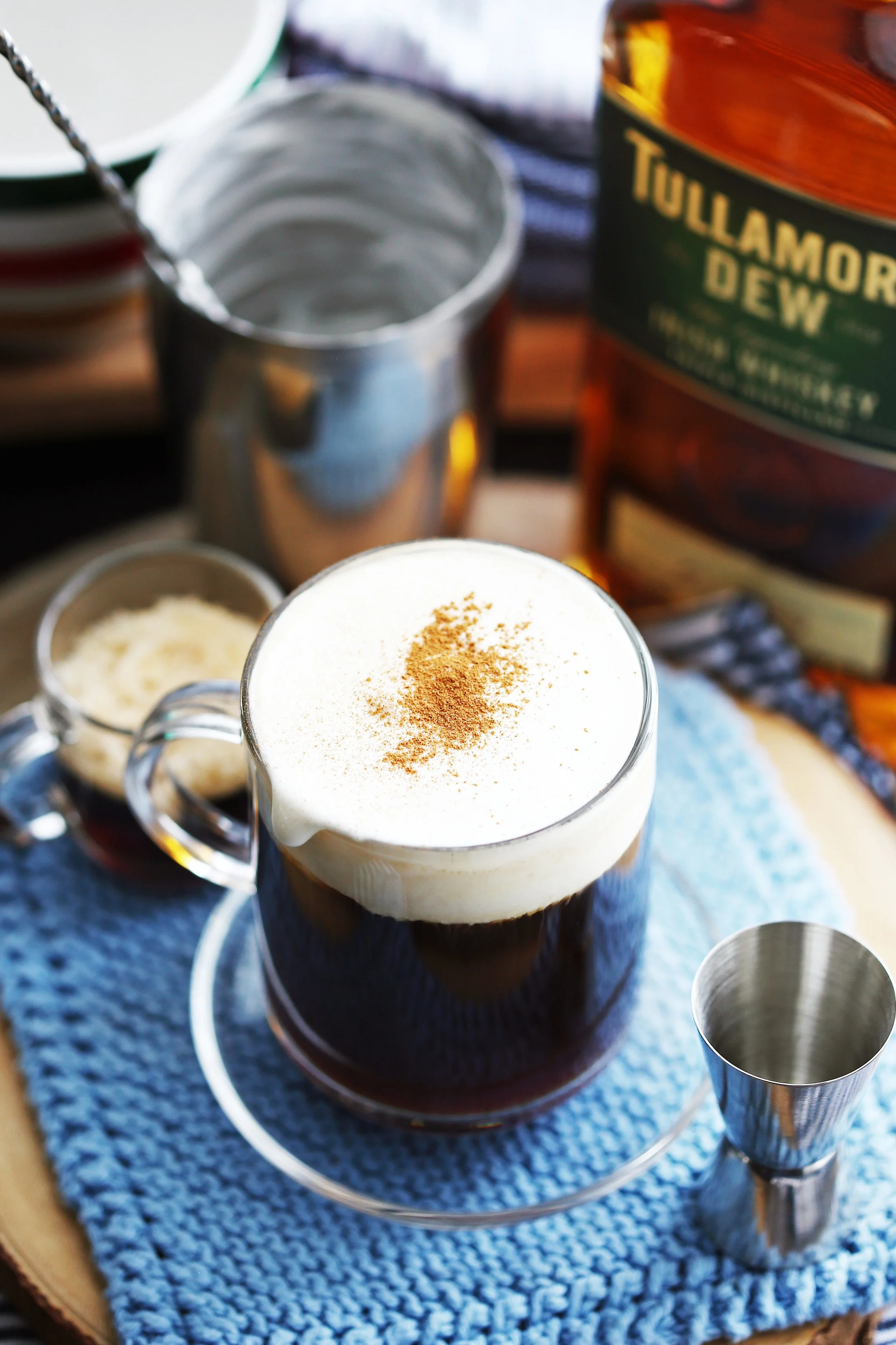 Maple Irish coffee topped with lightly whipped cream and ground cinnamon in a glass mug.