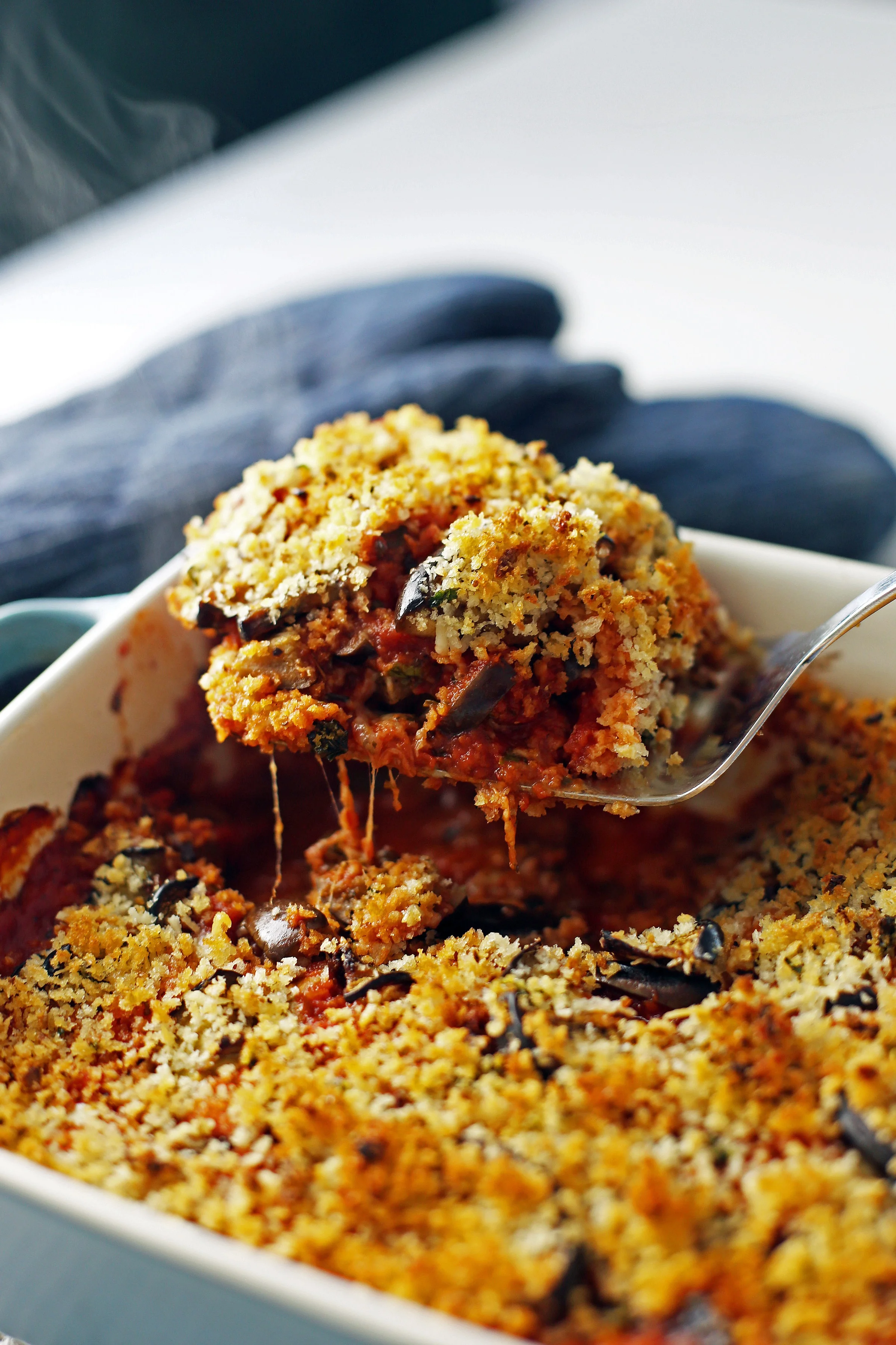 A piece of cheesy baked eggplant parmesan being lifted out of a casserole dish using a metal spatula.