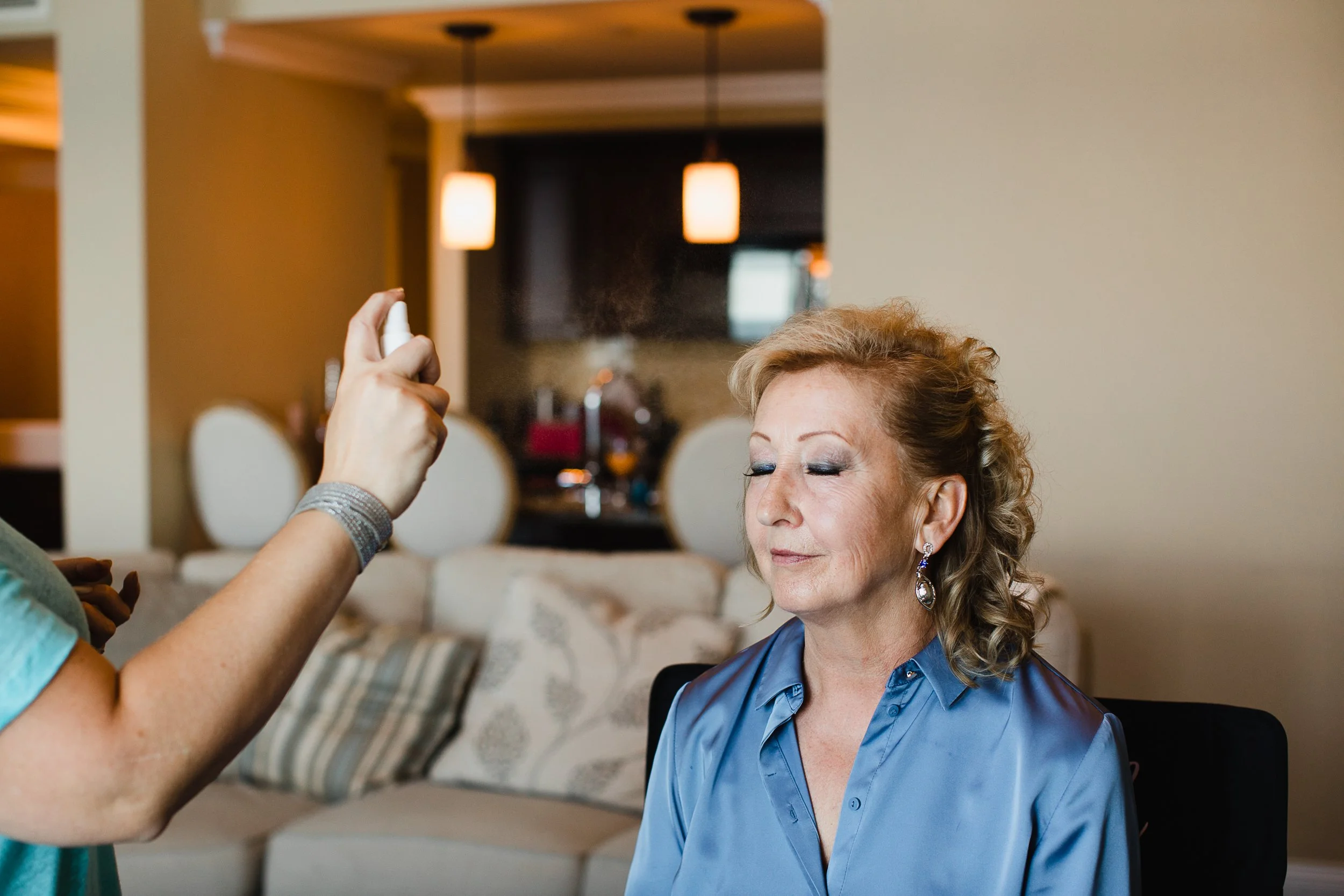 Makeup artist applying setting spray to mature client's face