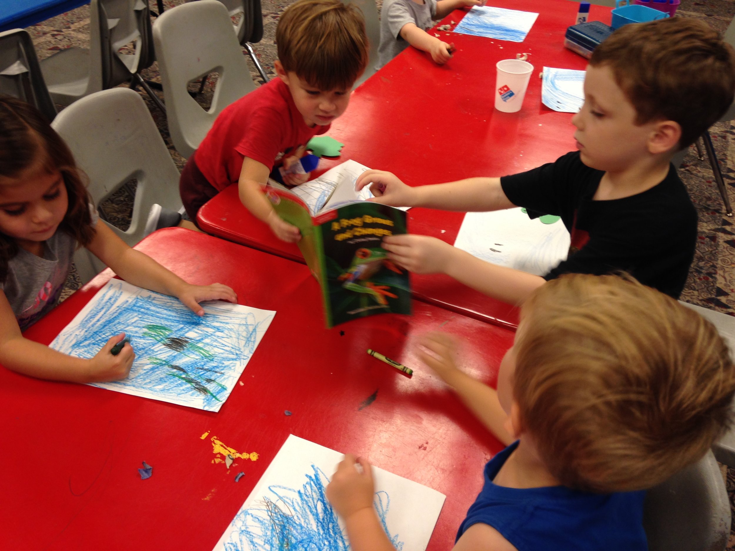 Studying the photos in the book to make sure they create a perfect habitat for construction paper frogs.