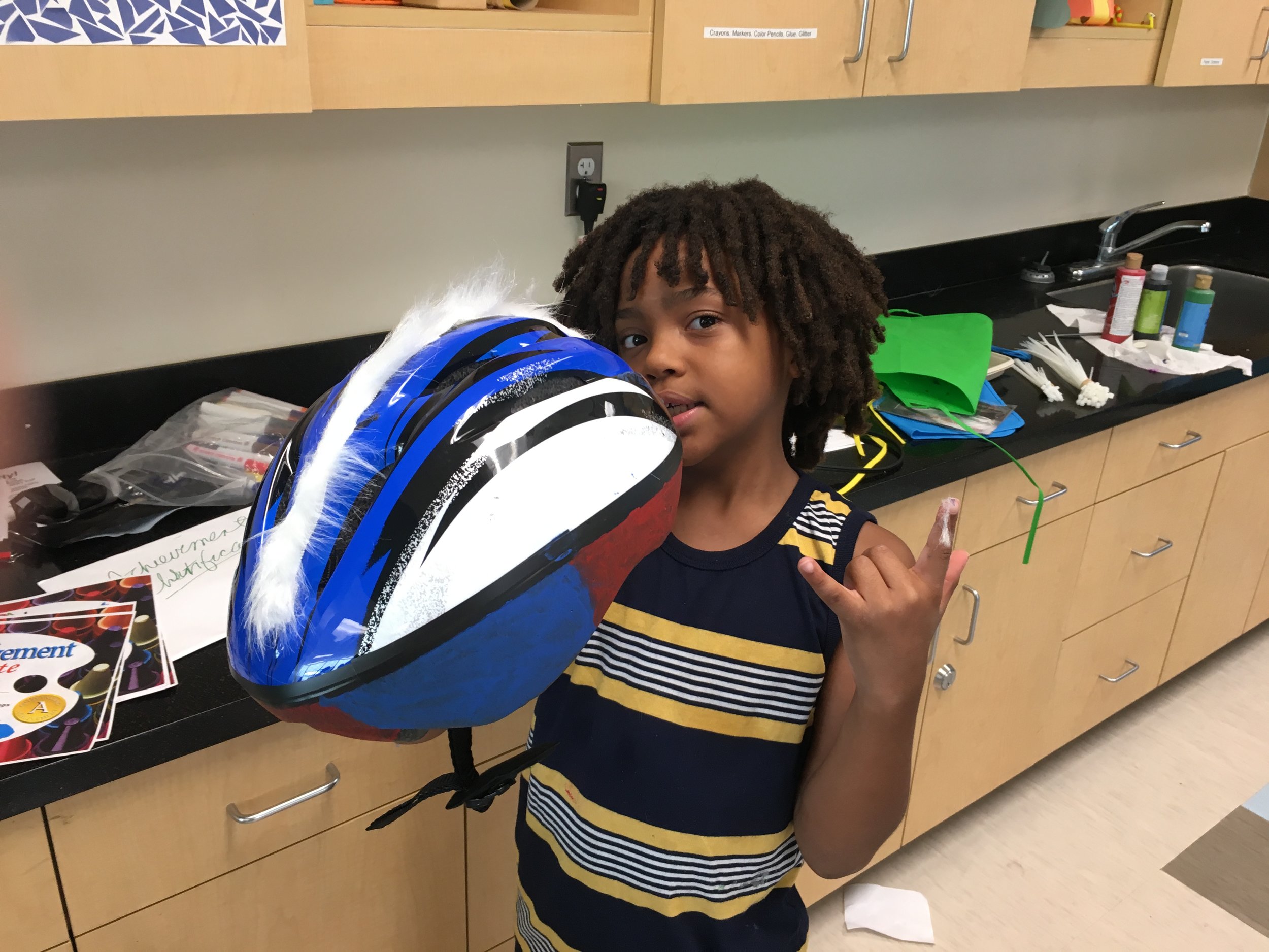 This student at Campbell Park chose white fun fur to accent a blue and white helmet. Fun Fur was attached with plastic zip ties or ribbon. Bicycle Helmets were sized during the student's introductory visit to the Dalí Museum. Helmets were then ordered. Before Helmets could be decorated, the fit required individual adjustment to chin straps and rear tension screws. During class each student was custom fit to the helmet that was their correct size and color choice. Then the fun really began! 