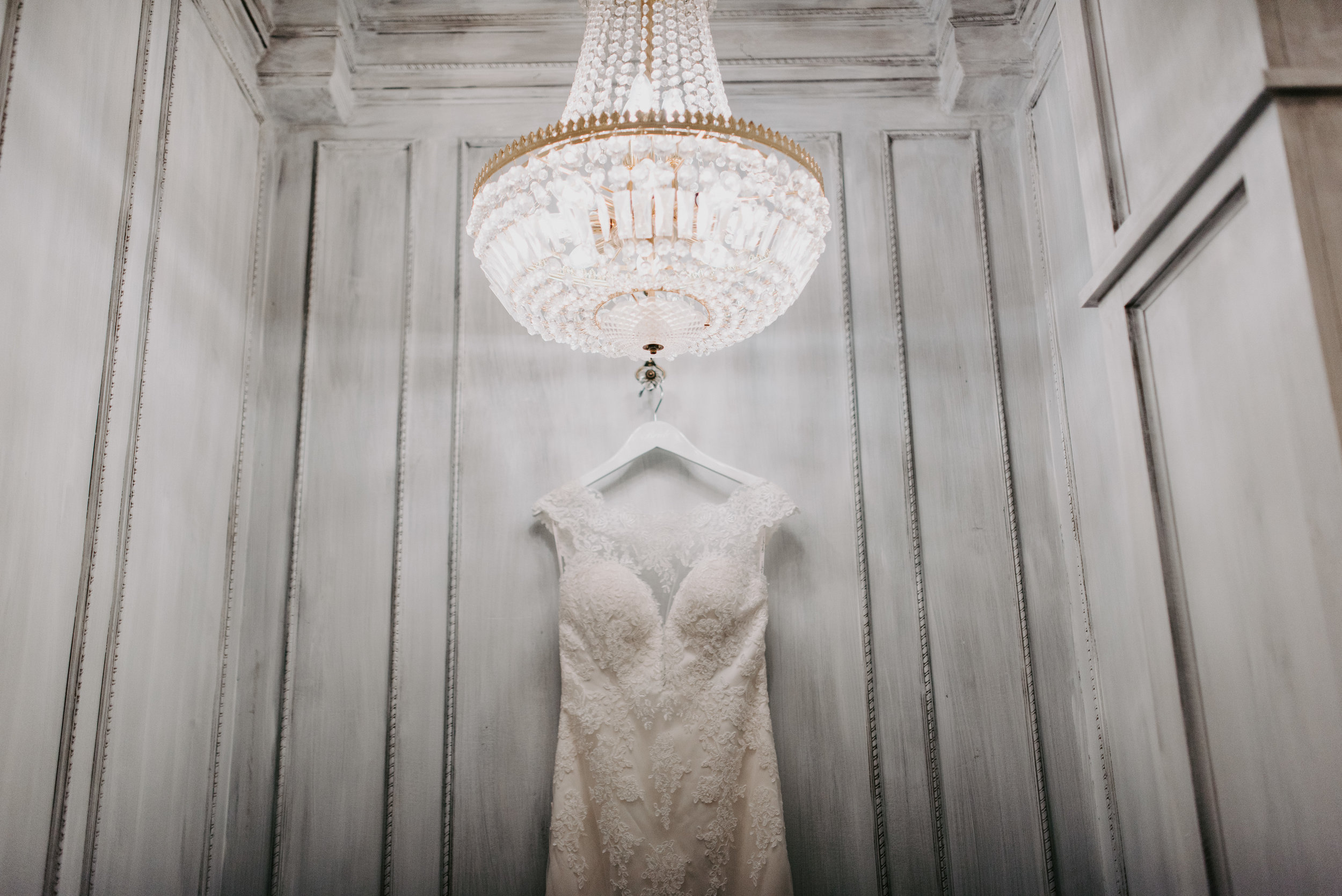 lace wedding dress under chandelier with white walls