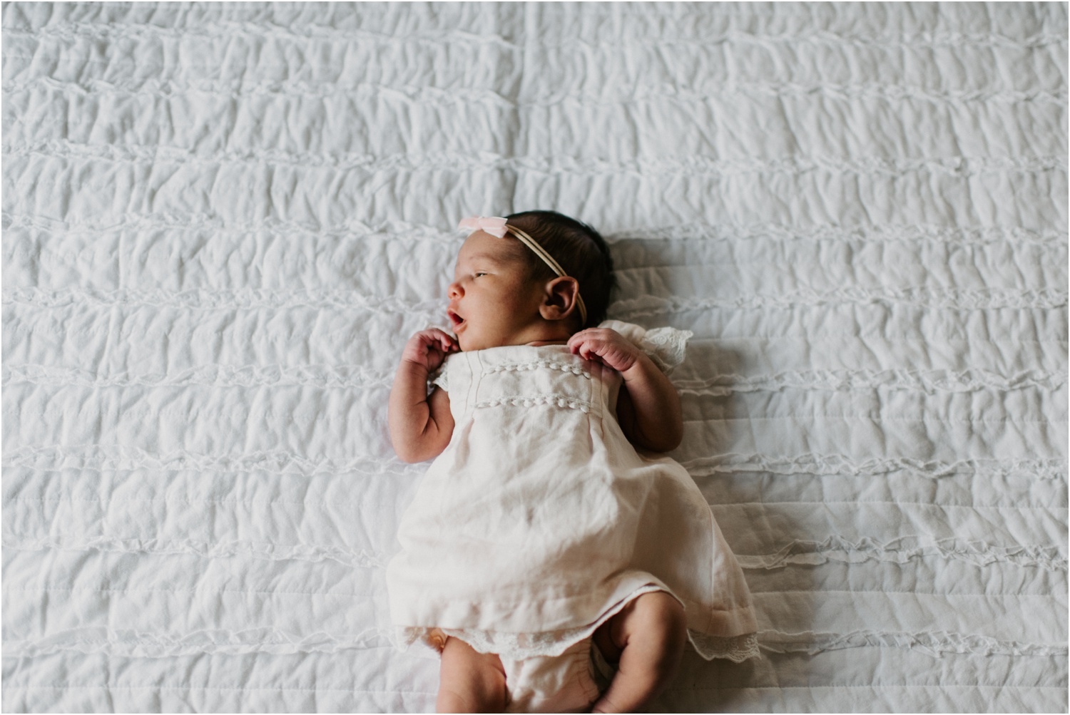 newborn laying on white bed with pink bow