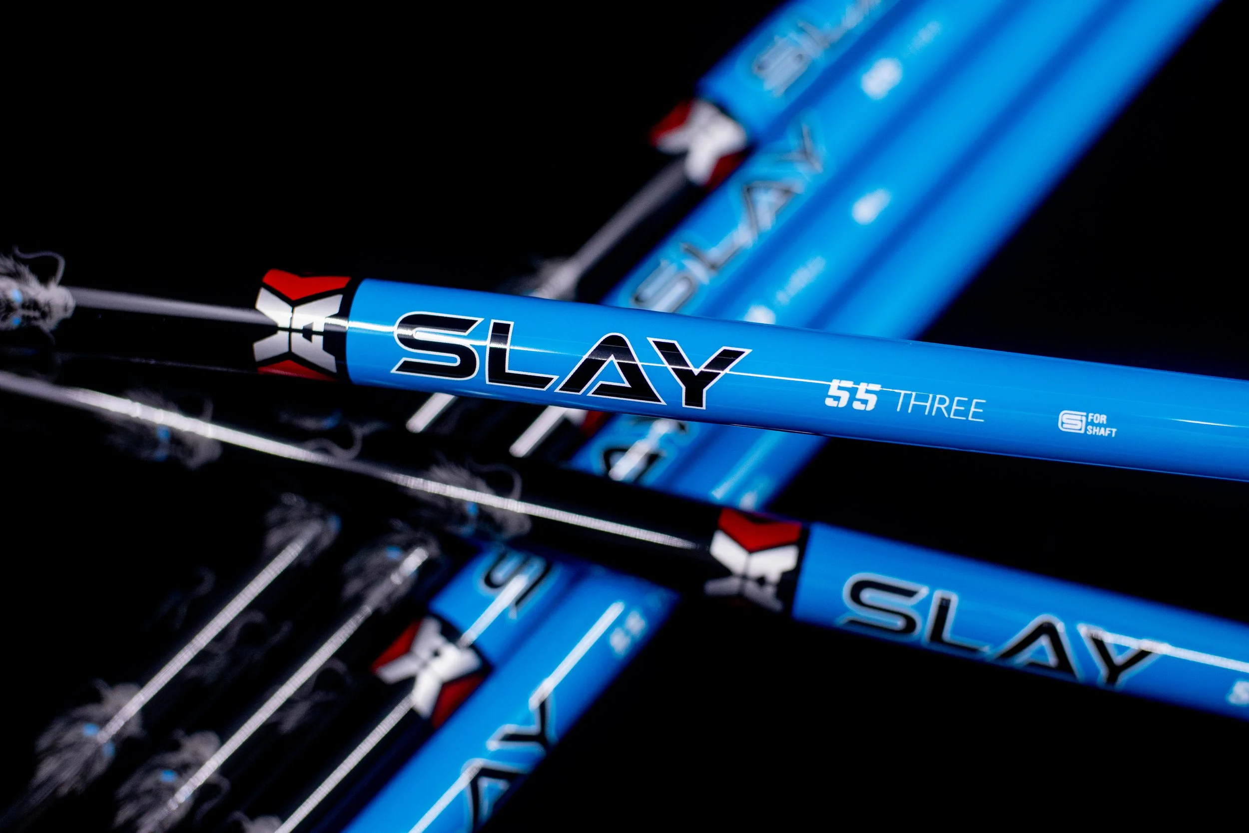 Close-up of blue golf club shafts with the word 'SLAY' printed on one, background is black.