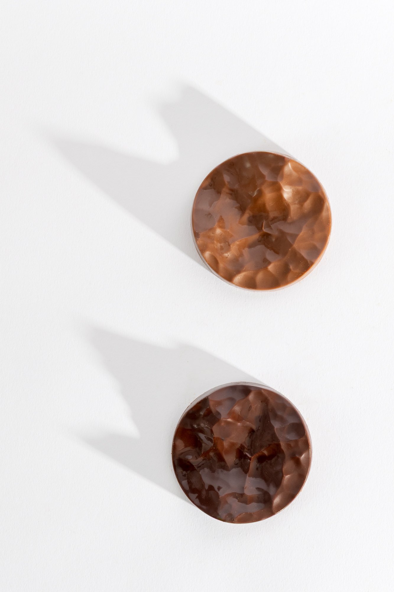 Three round, marbled chocolate pieces arranged vertically on a white background, casting shadows.