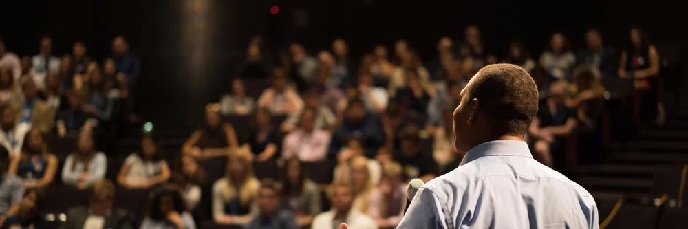 Stephen Rowe speaking to a large audience, seen from behind the stage