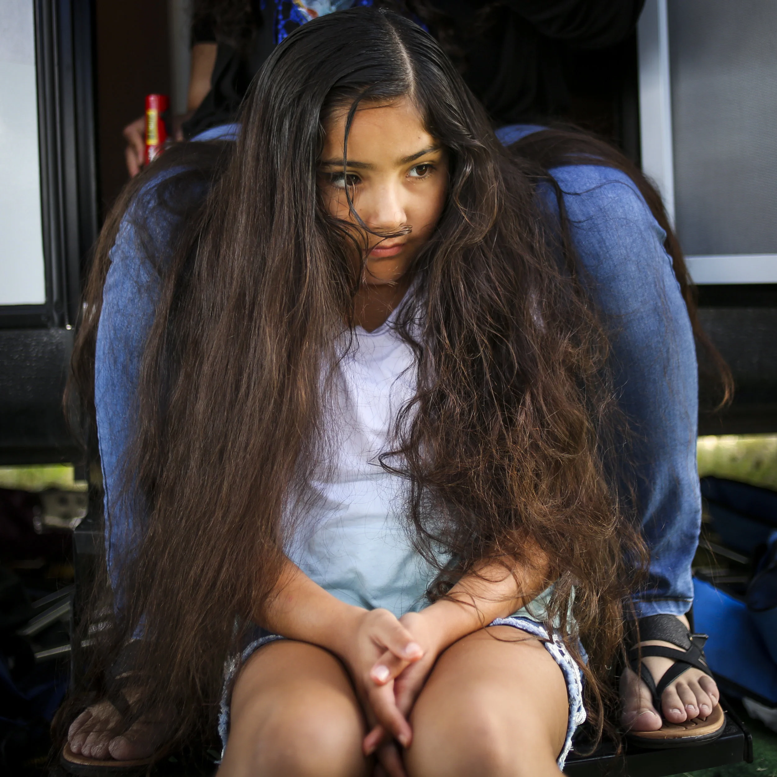  Esther Montoya, 8, sits between her mother’s legs on the stairs of their camper waiting for her hair to be braided at the 121st Arlee Celebration in Arlee, Montana on July 4, 2019. Hair is just the first step in the long process of getting prepared 
