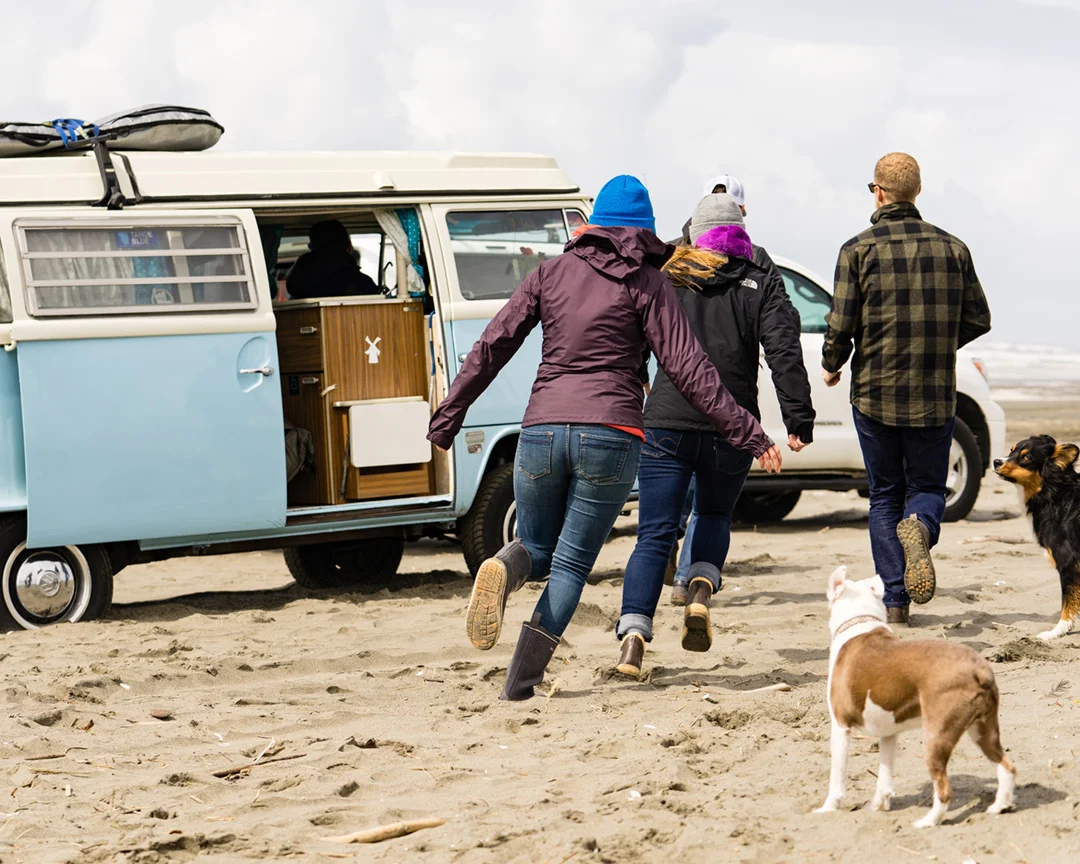 group of friends running toward a camper van on the beach