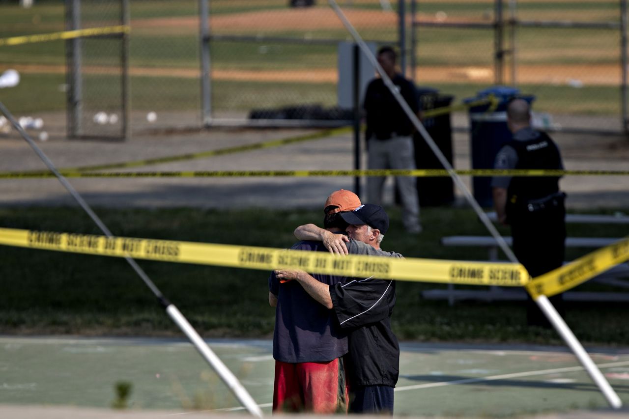 Two people hug in front of police crime scene tape following a shooting