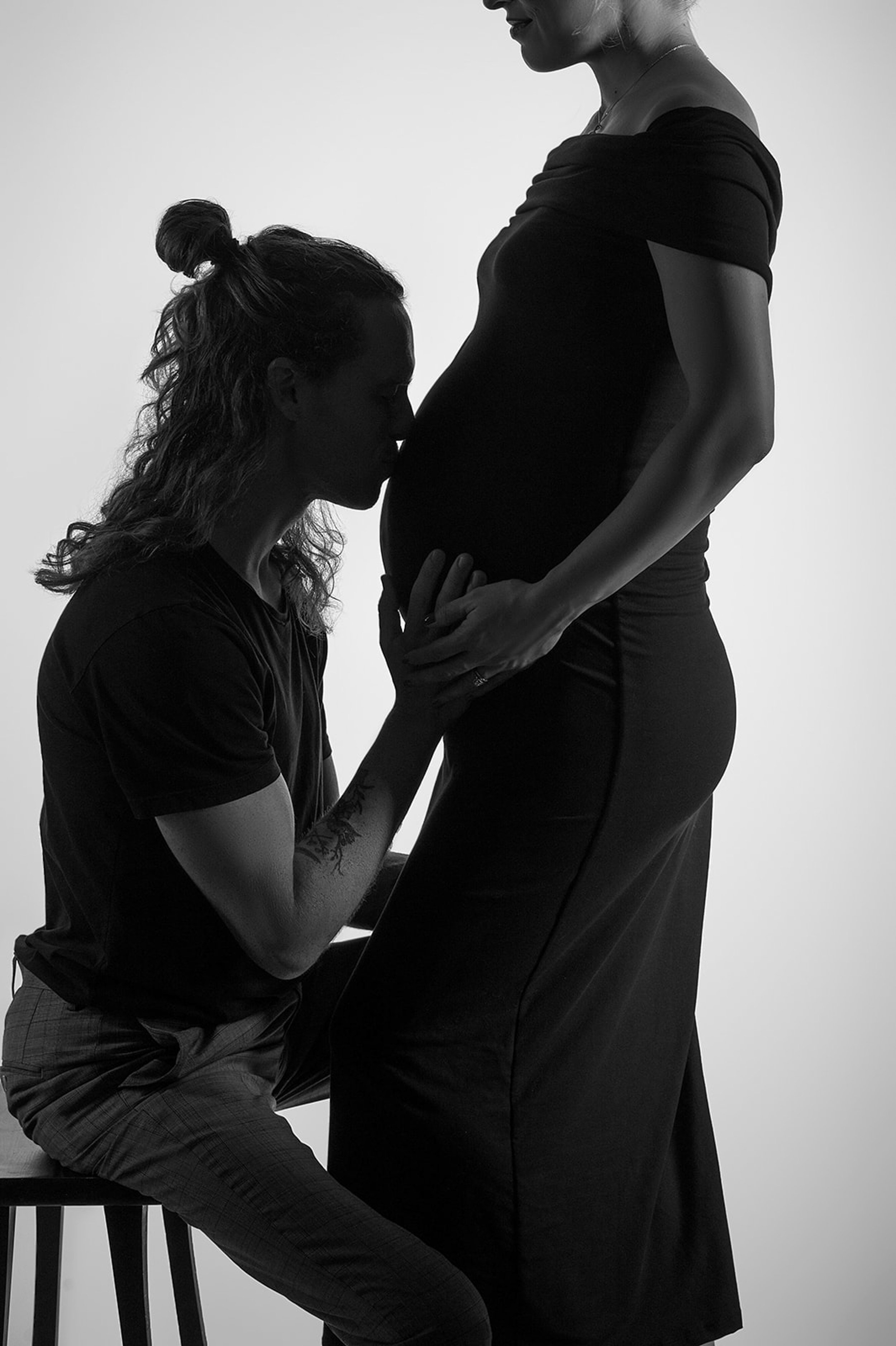  A silhouette of a young couple expecting a baby. A father to be is kissing the bum of the expecting mother to be. 