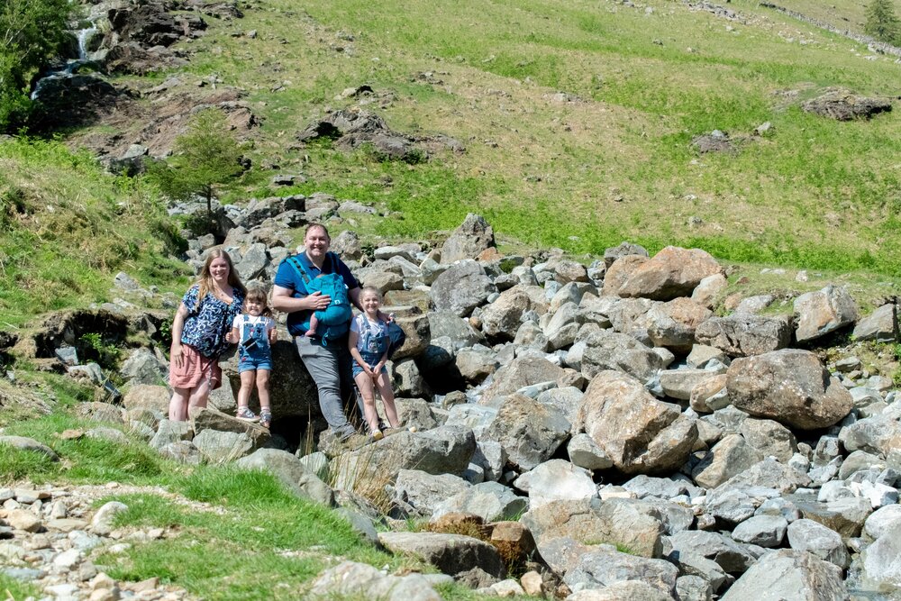 The Hassan family are stood on a rocky hillside above Buttermere with a small beck flowing down to their left.