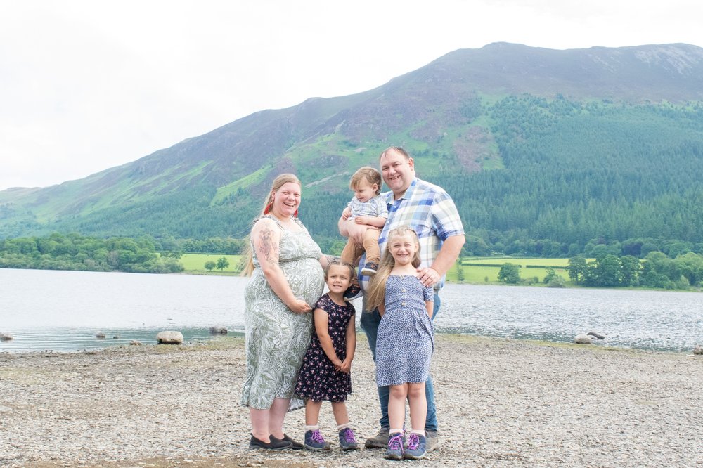 The Hassan family are on the lakeshore of Bassenthwaite together with Naomi pregnant and the lakeland fells behind them to take maternity photos.