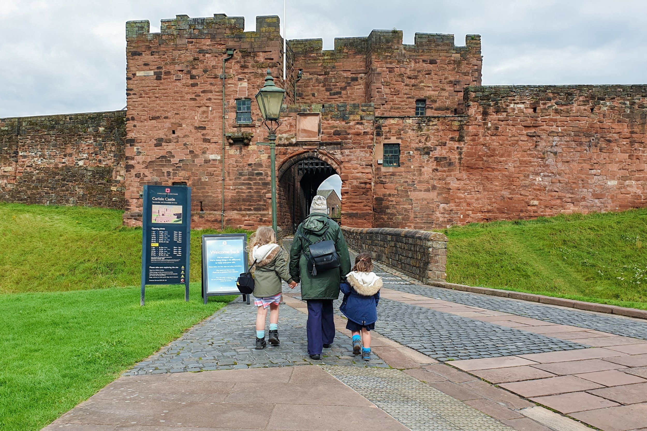 Squidgy and Pickle are holding their Grandma's hand and walking towards the entrance archway to Carlisle castle.