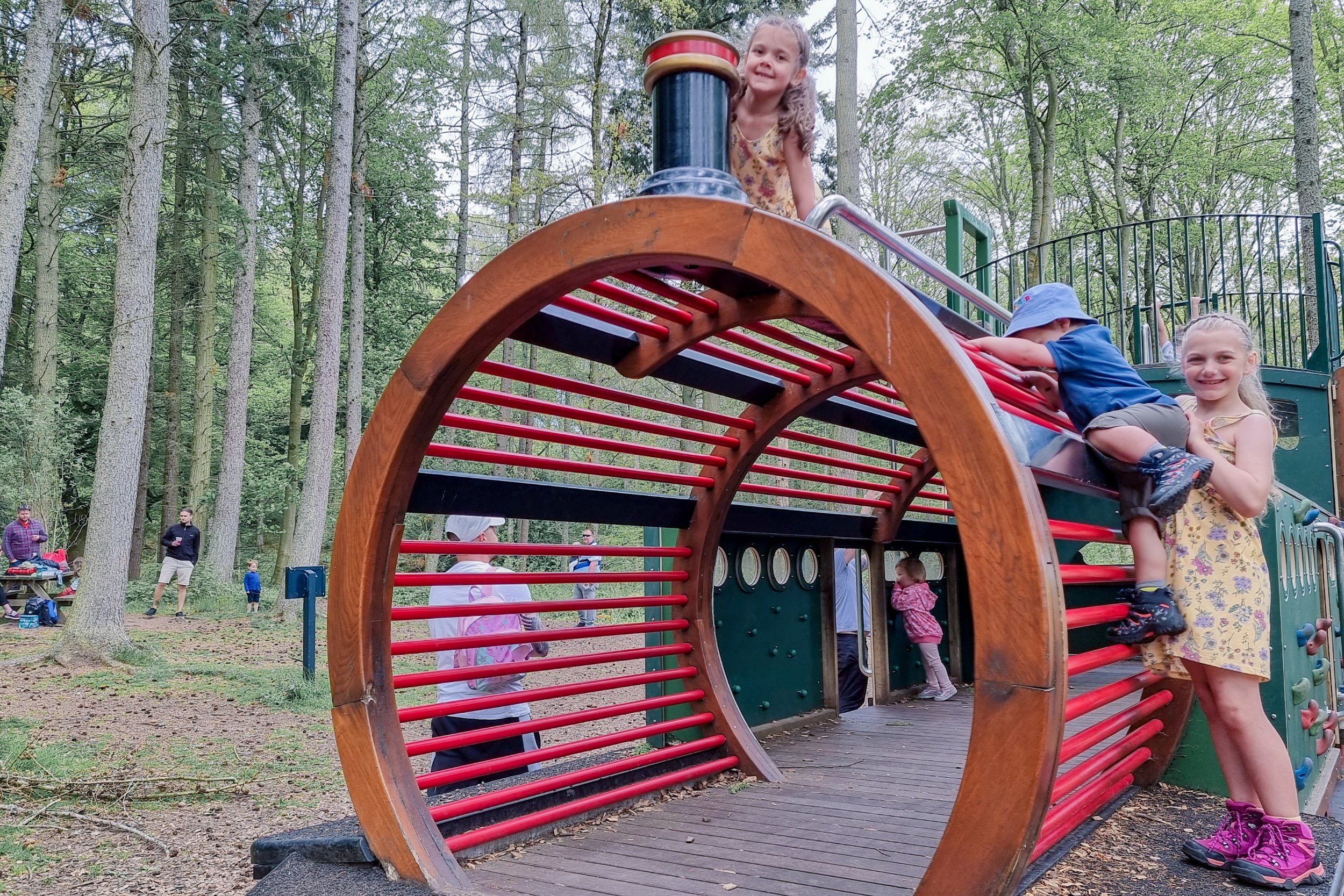 An image of the front of the play train. You can see Pickle on top, with Squidgy and Munchkin climbing the side. It is situated in a woodland setting.
